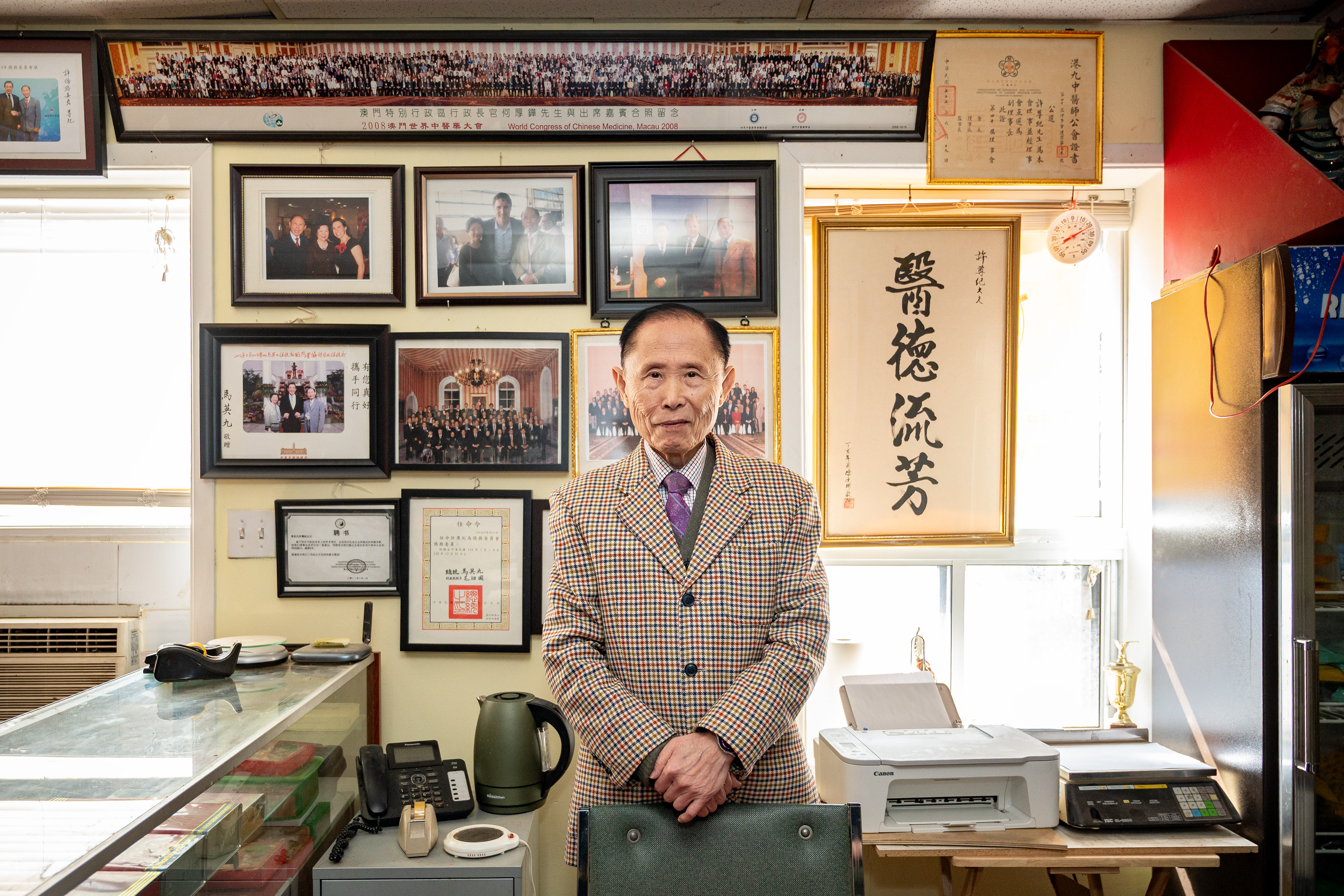 Chun Kee Hui pose fièrement devant des photos avec des dignitaires dans son bureau privé  Chun Kee Hui stands proudly in front of photos with dignitaries in his private office  許遵紀驕傲地站在私人辦公室內，身後是與政要合影的照片
