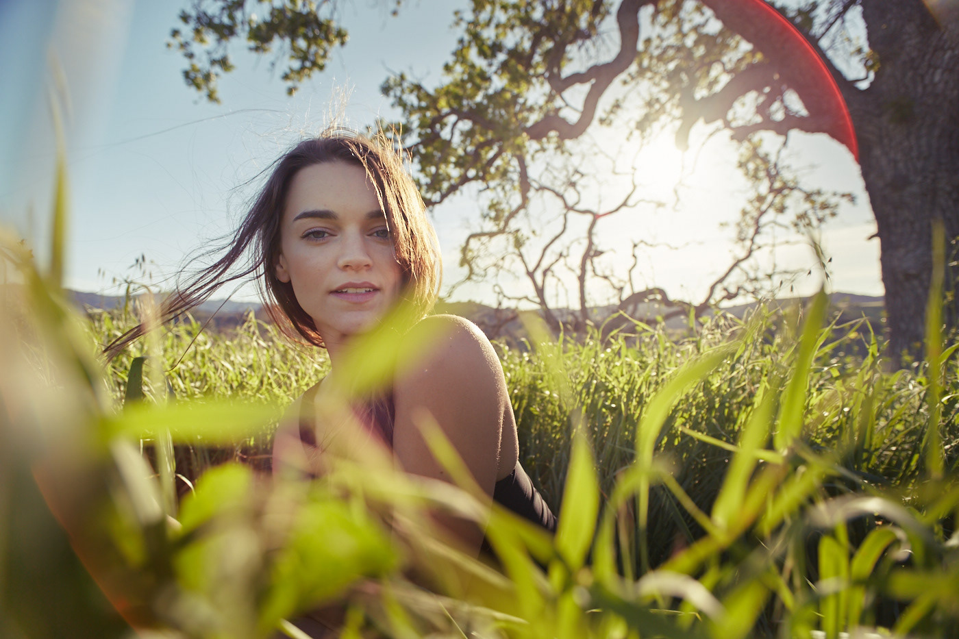Beautiful woman sitting in tall grass.  Wind blowing. Photo by Modern Human