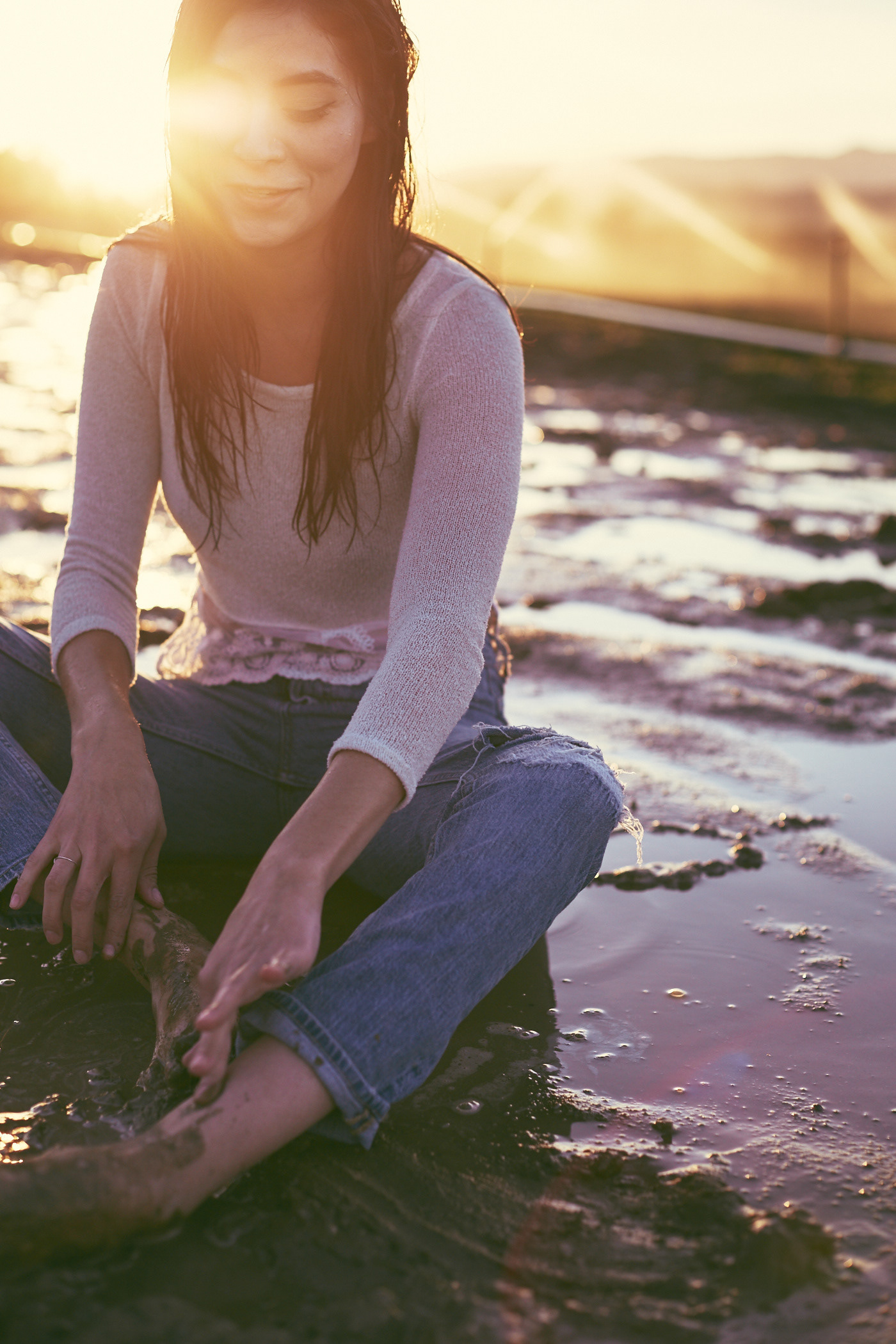 Beautiful woman sits in the mud, drenched.  She smiles.  Photo by Modern Human