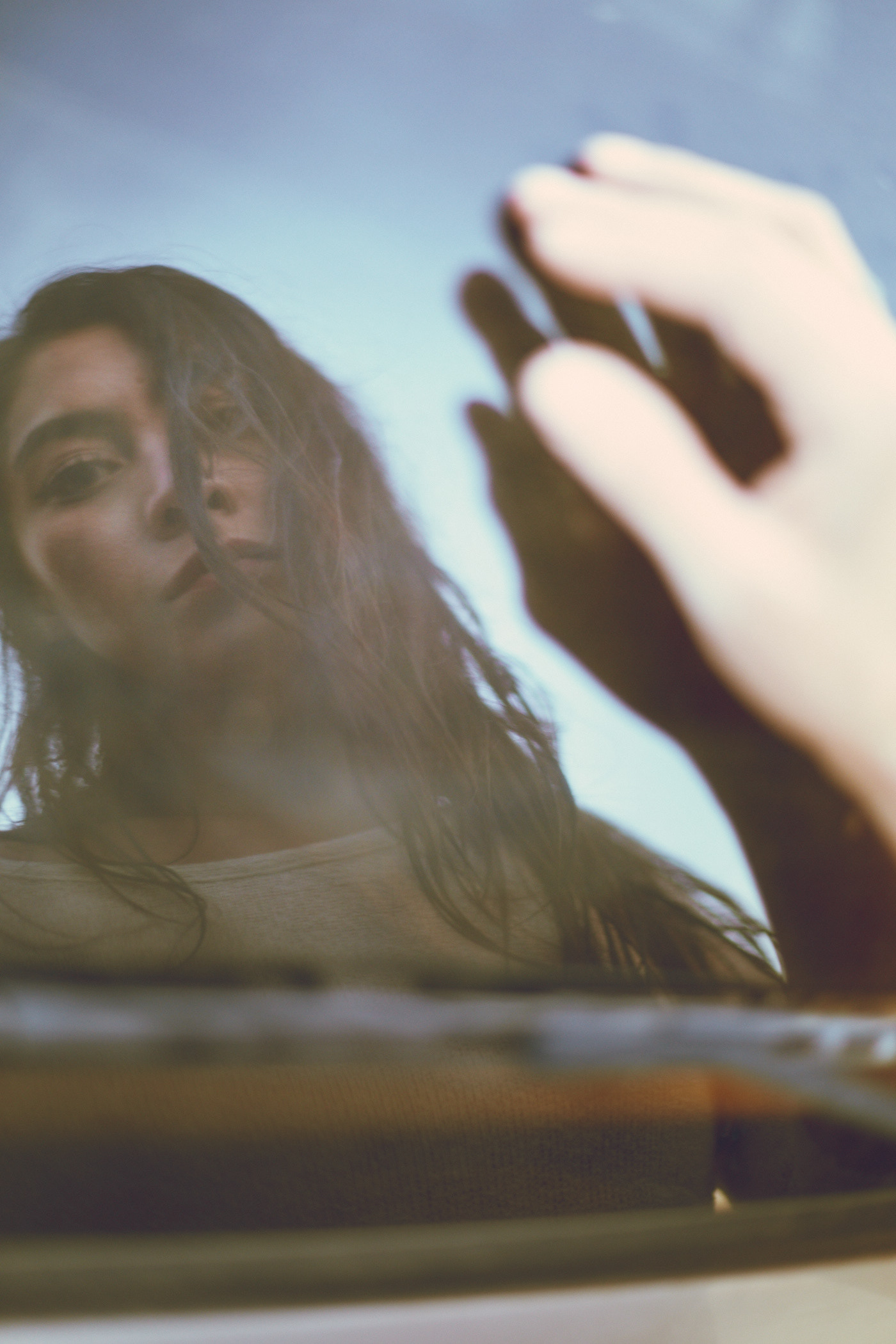 Beautiful woman, soaking wet, looks in the back window of a car.  Her reflection his thoughtful.  Photo by Modern Human