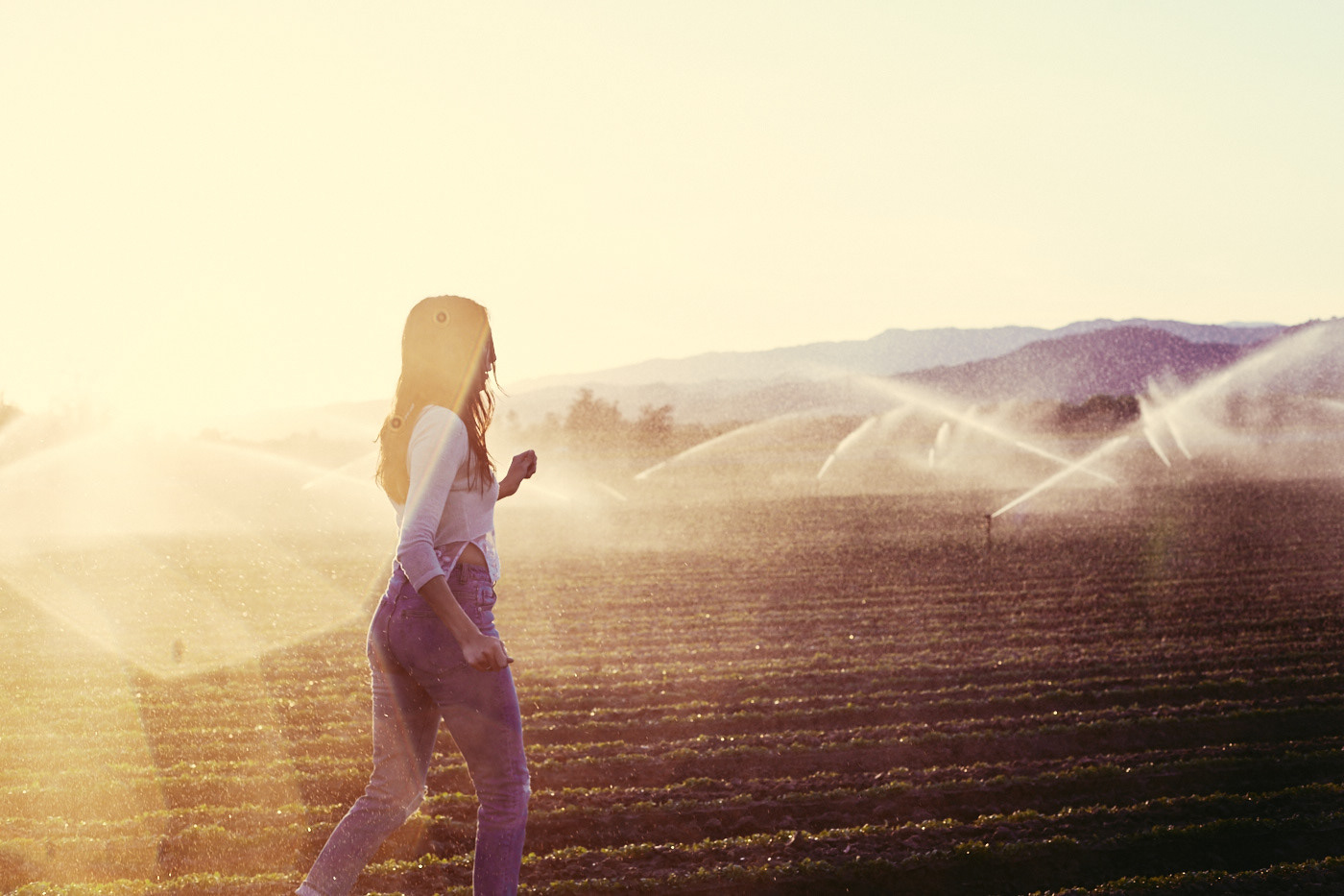 Beautiful woman runs through sprinklers in field.  Photo by modern human