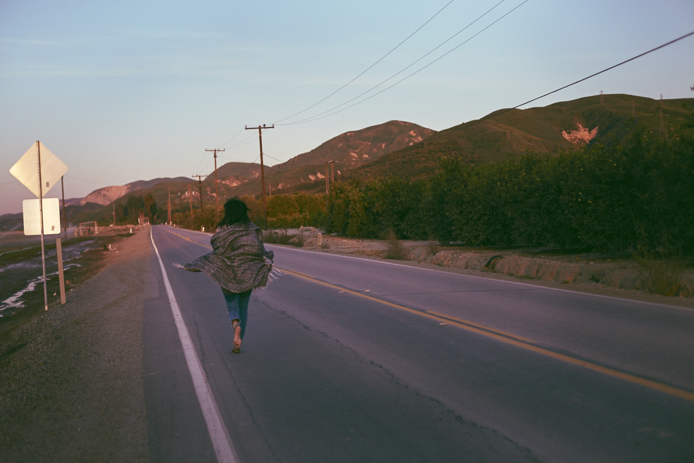 Beautiful woman runs away, down a vacant highway.  Mountains loom in the distance.  Photo by Modern Human