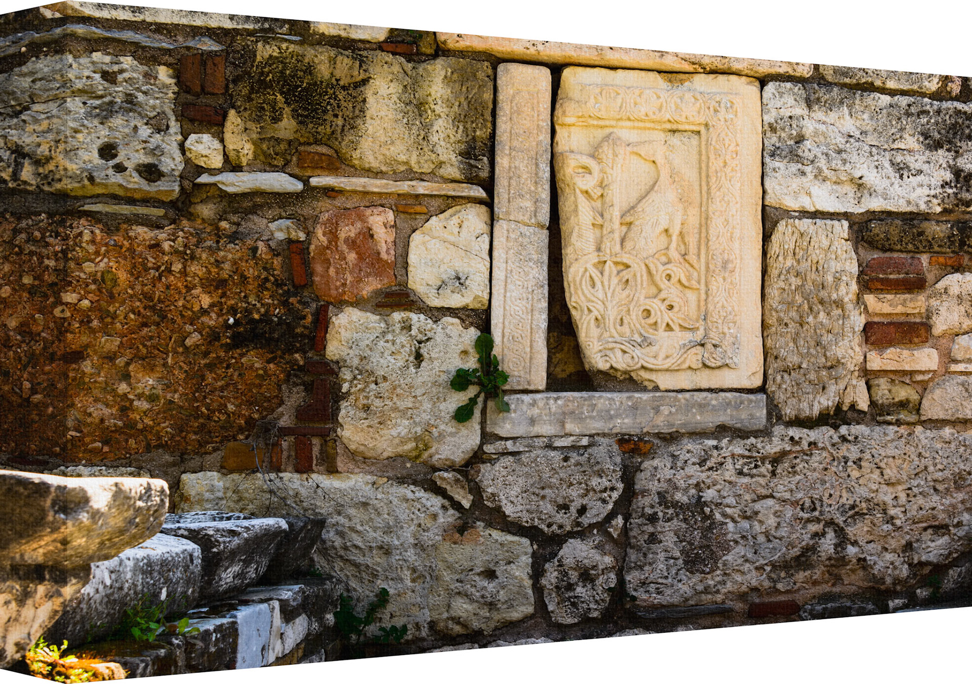 Building Ancient Stone Walls...The Canvas image entitled 'Tears of Stone' shows a section of an old stone wall with various elements. There is a rectangular carved stone relief embedded in the wall, featuring intricate floral or vegetal designs and what appears to be a figure in the center, possibly of historical or archaeological interest. The surrounding stones and bricks are of different sizes and shapes, indicating repairs or construction from different periods. A small green plant grows from between the stones on the lower left side, adding a touch of life to the scene. This image captures the texture and history embedded in ancient architecture, as well as the contrast between the enduring craftsmanship of the relief and the natural elements that slowly reclaim human-made structures over time.