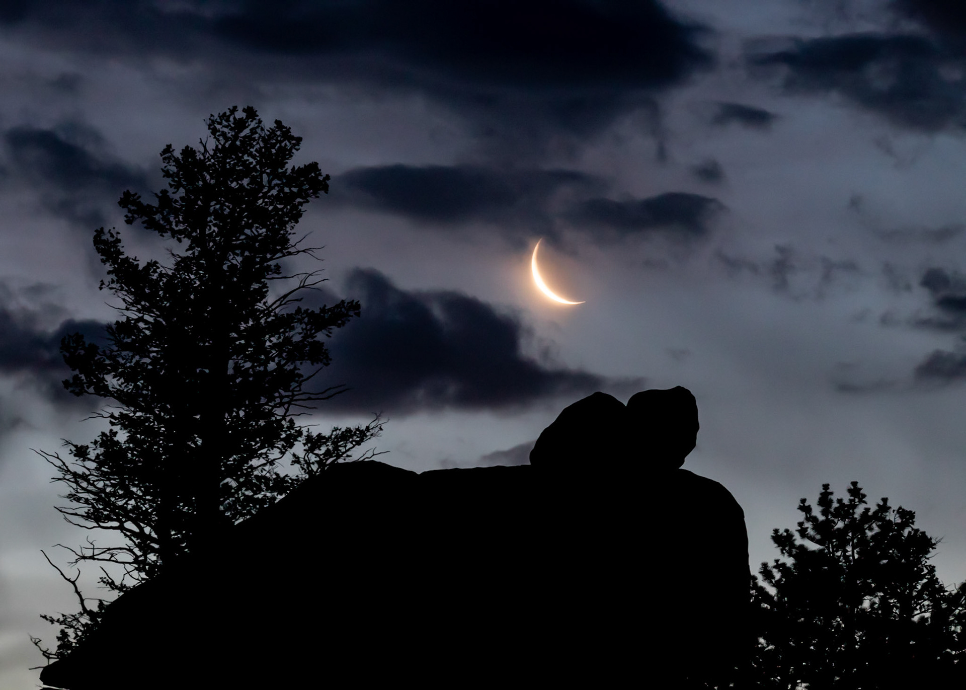 Crescent moonset over silhoutted rocks