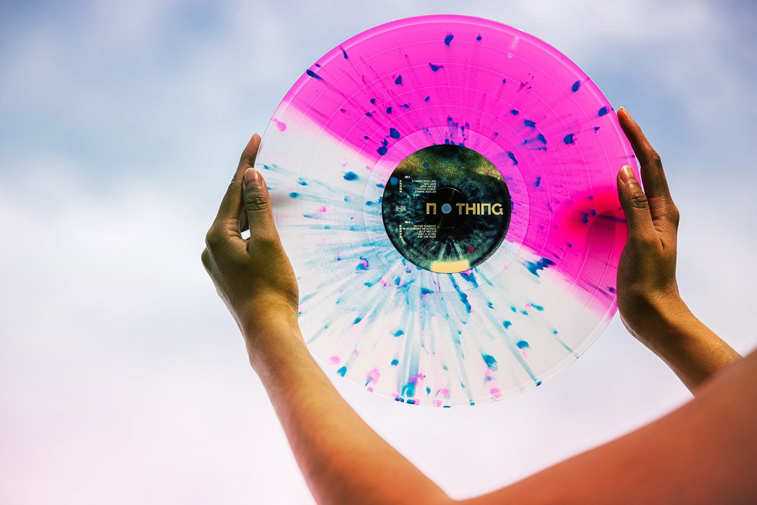 hands holding up a pink splatter vinyl record against the sky, vinyl record photography by Chris Stokes