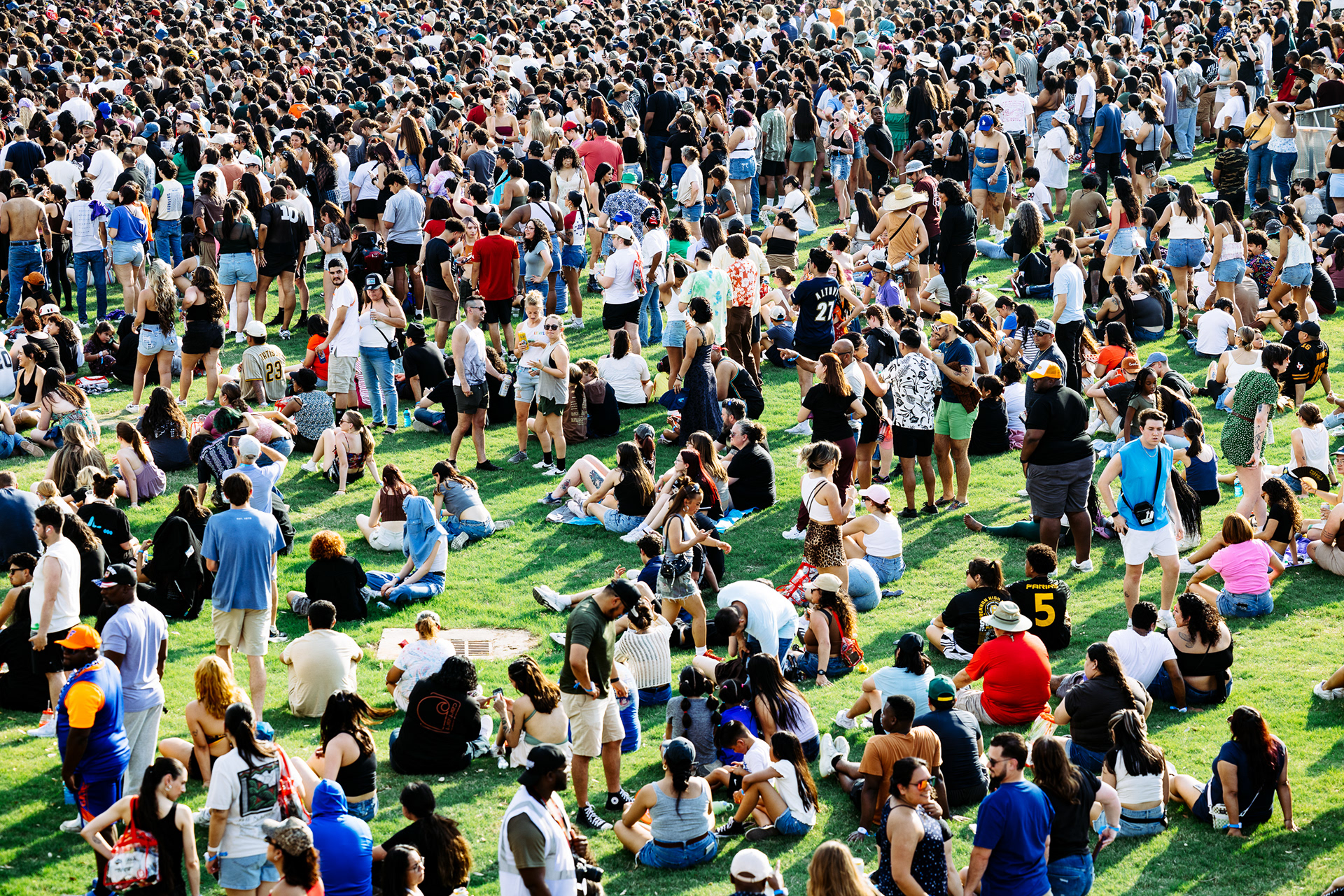 huge crowd gathered on a grass lawn at a music festival, photographed from above by Chris Stokes