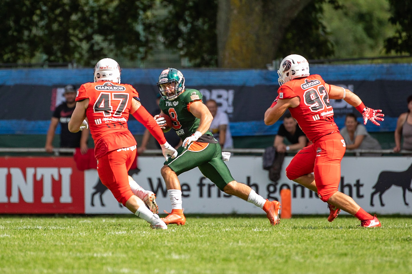 8 Victor Ferrier (grün) gegen 47 Jonathan Falk und Adam Roszowski (rot von links) im Spiel der Kiel Baltic Hurricanes (grün) gegen die Braunschweig New Yorker Lions (rot) am 03.08.19 im Kilia Stadion in Kiel