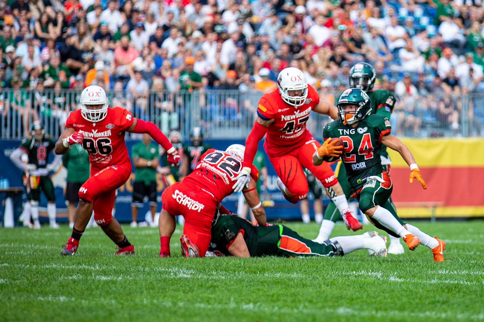 24 Fritjof Richter (grün) läuft der Braunschweiger Defense weg. 96 Samuel Kargel, 92 Adam Roszkowski und 47 Jonathan Falk im Spiel der Kiel Baltic Hurricanes (grün) gegen die Braunschweig New Yorker Lions (rot) am 03.08.19 im Kilia Stadion in Kiel