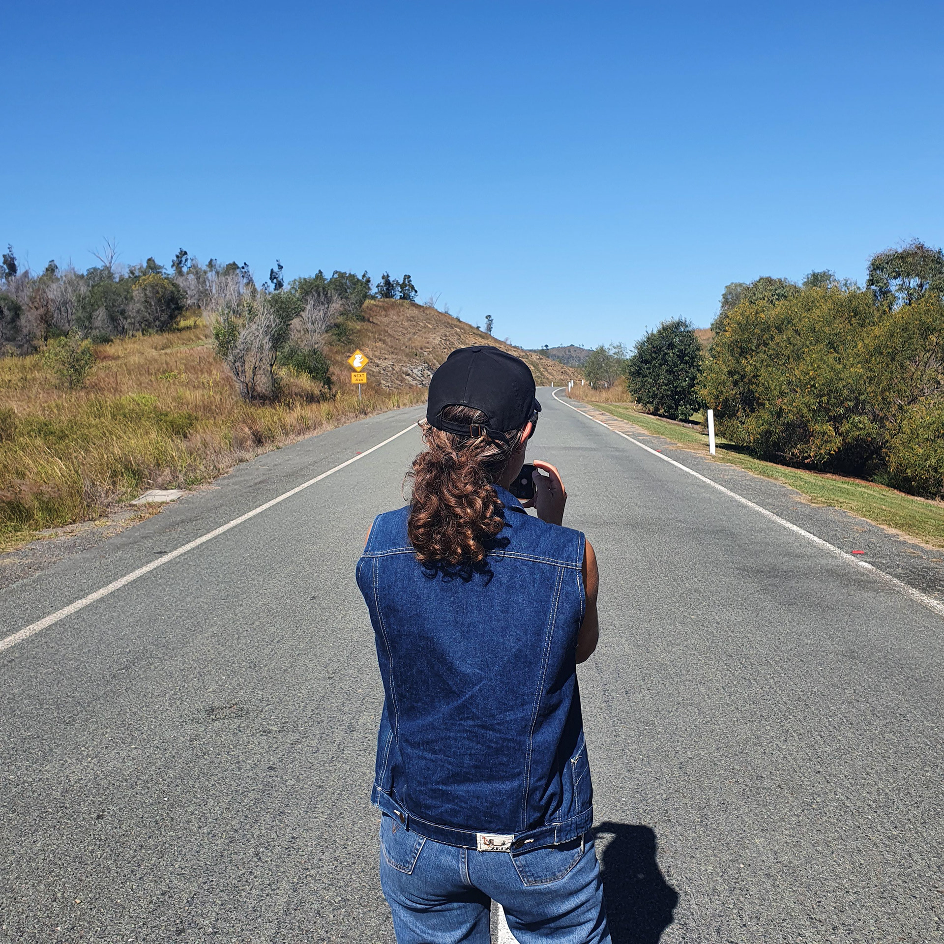 REBECCA ROSS, 2021; IMAGE DESCRIPTION: PONYTAILED PERSON TAKING PHOTO OF LONG STRETCH OF ROAD.