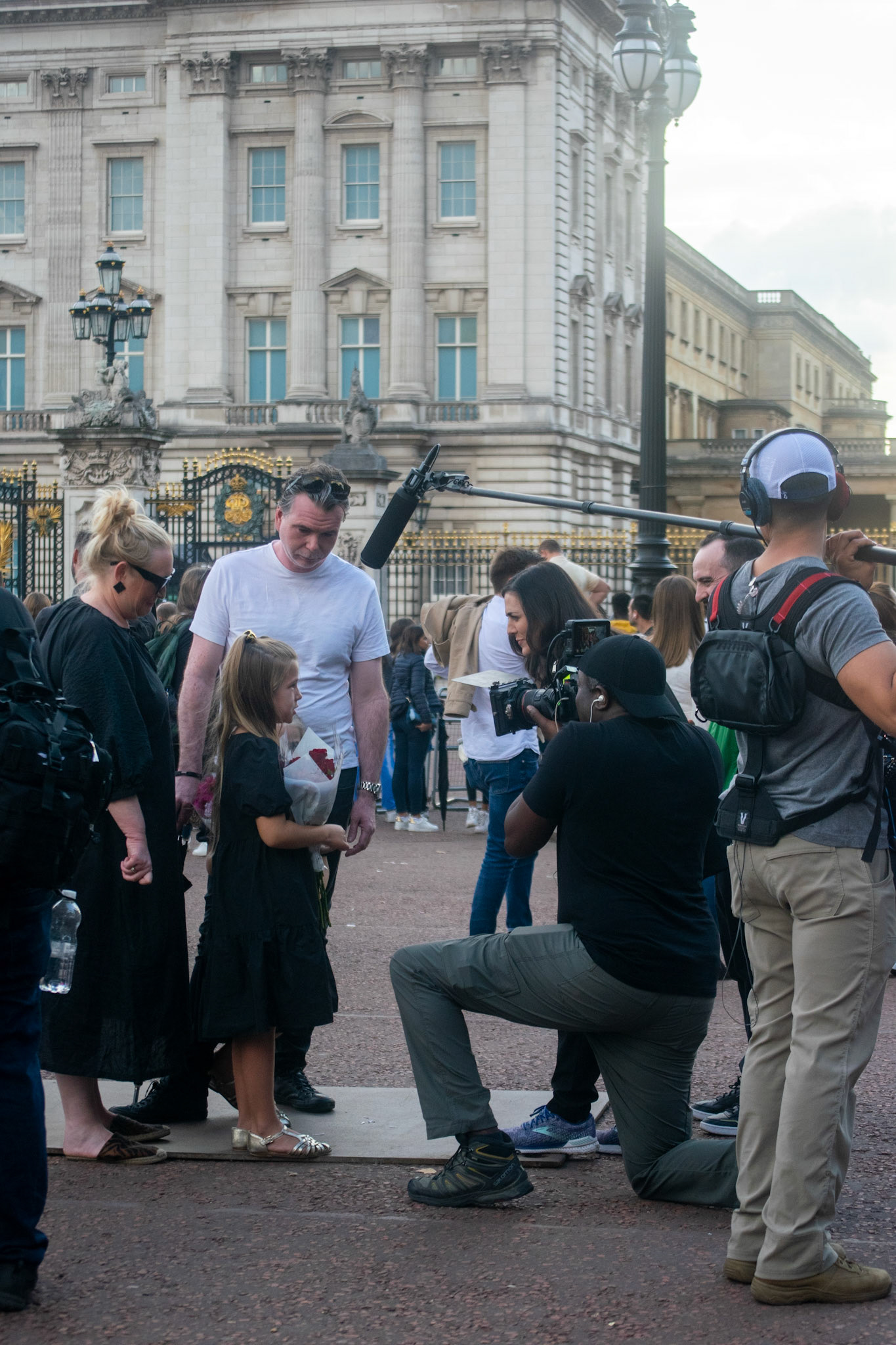 A little girl talks to a reporter dressed in black with a bouquet in her hands.