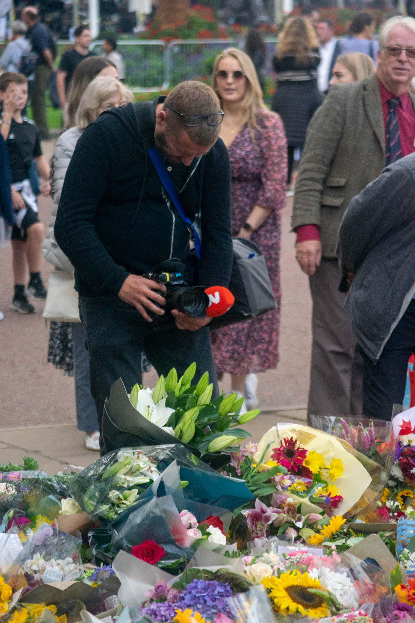 A cameraman recording a pile of flowers outside Buckingham palace.