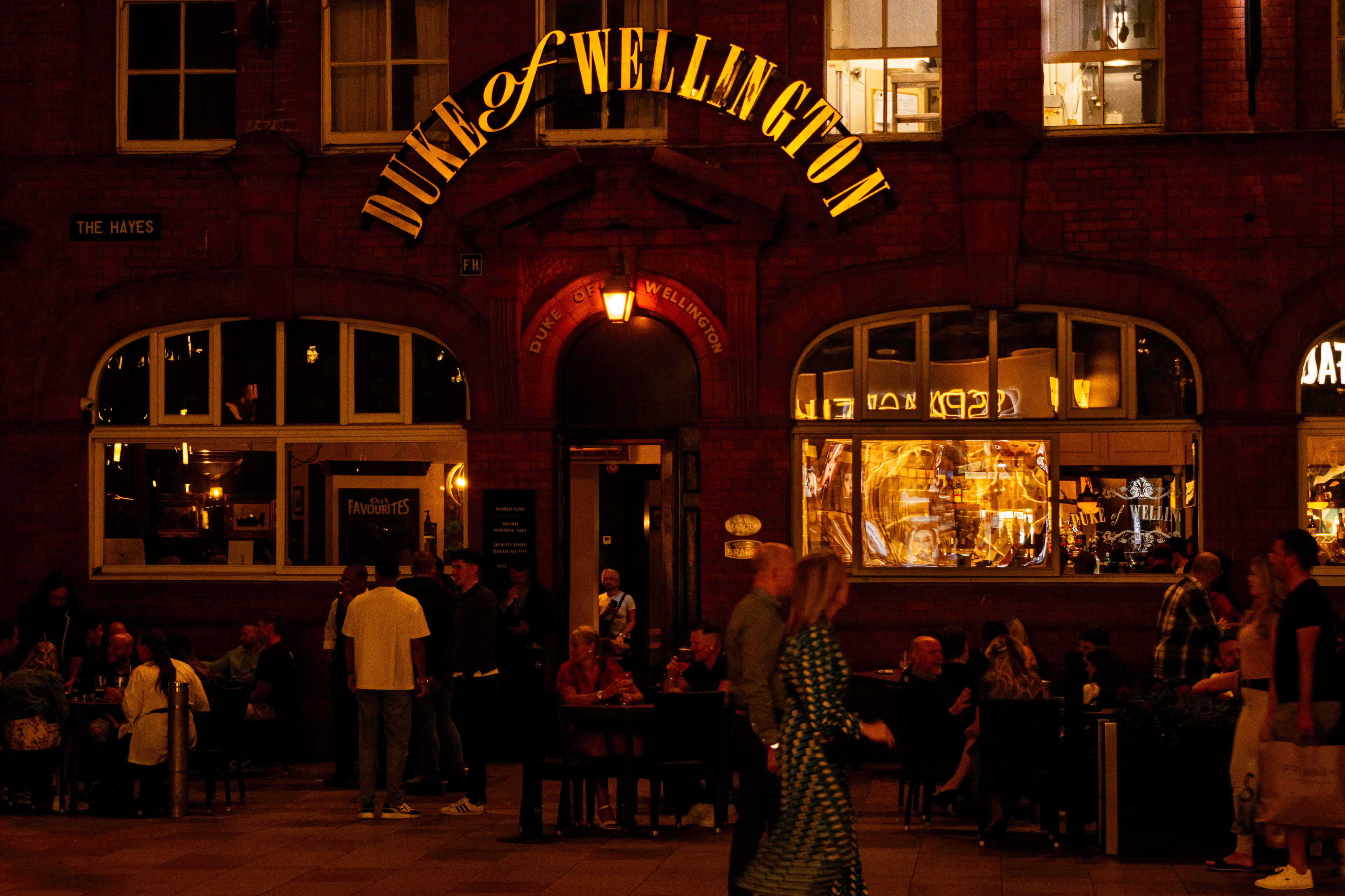 A couple walks by as the people enjoy a weekend night at the pub in the background.