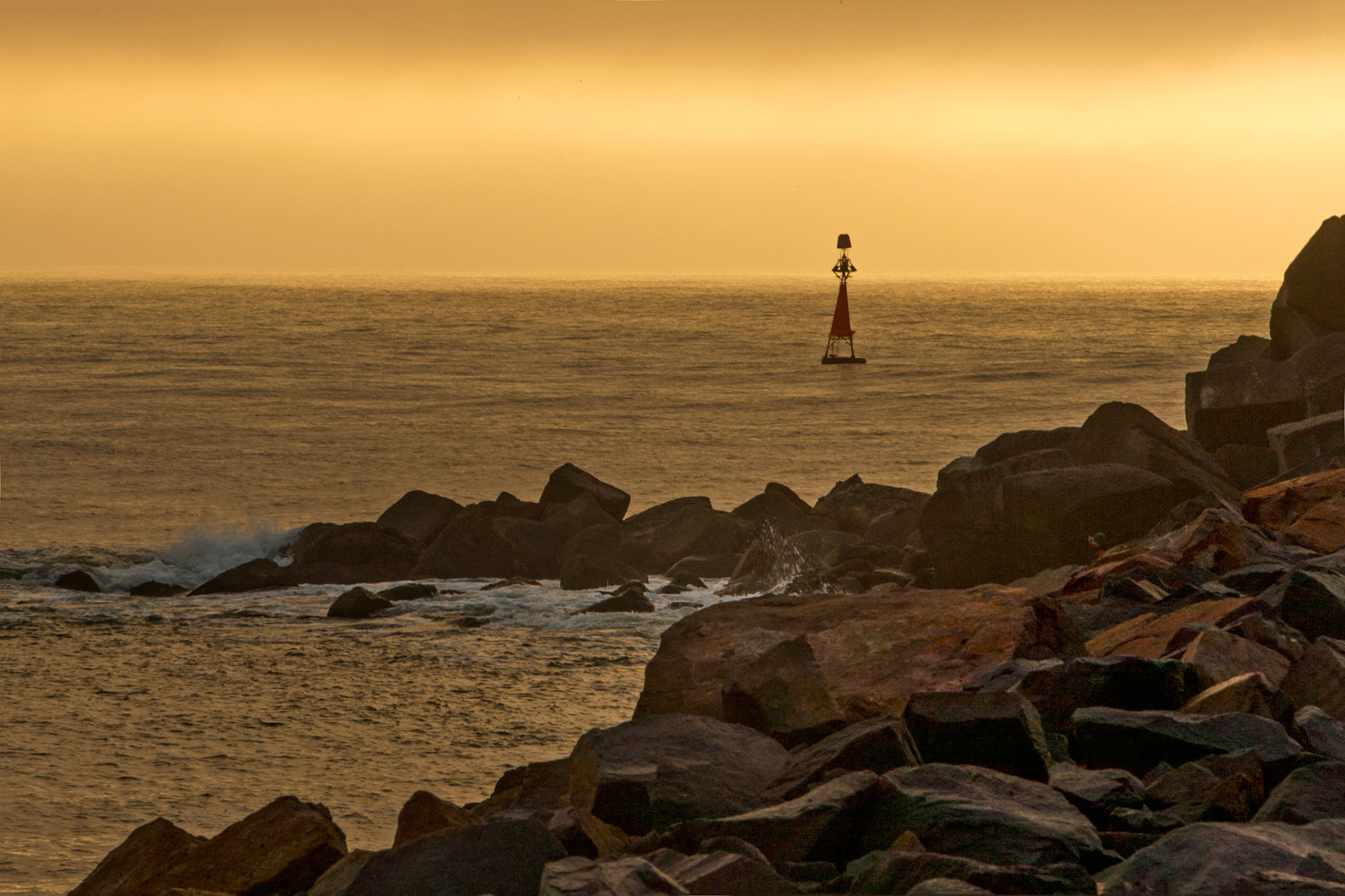 An early morning shot of the buoy and rocks on Macquarie pier leading into Newcastle port, with the rising sun yellowing the misty sky.