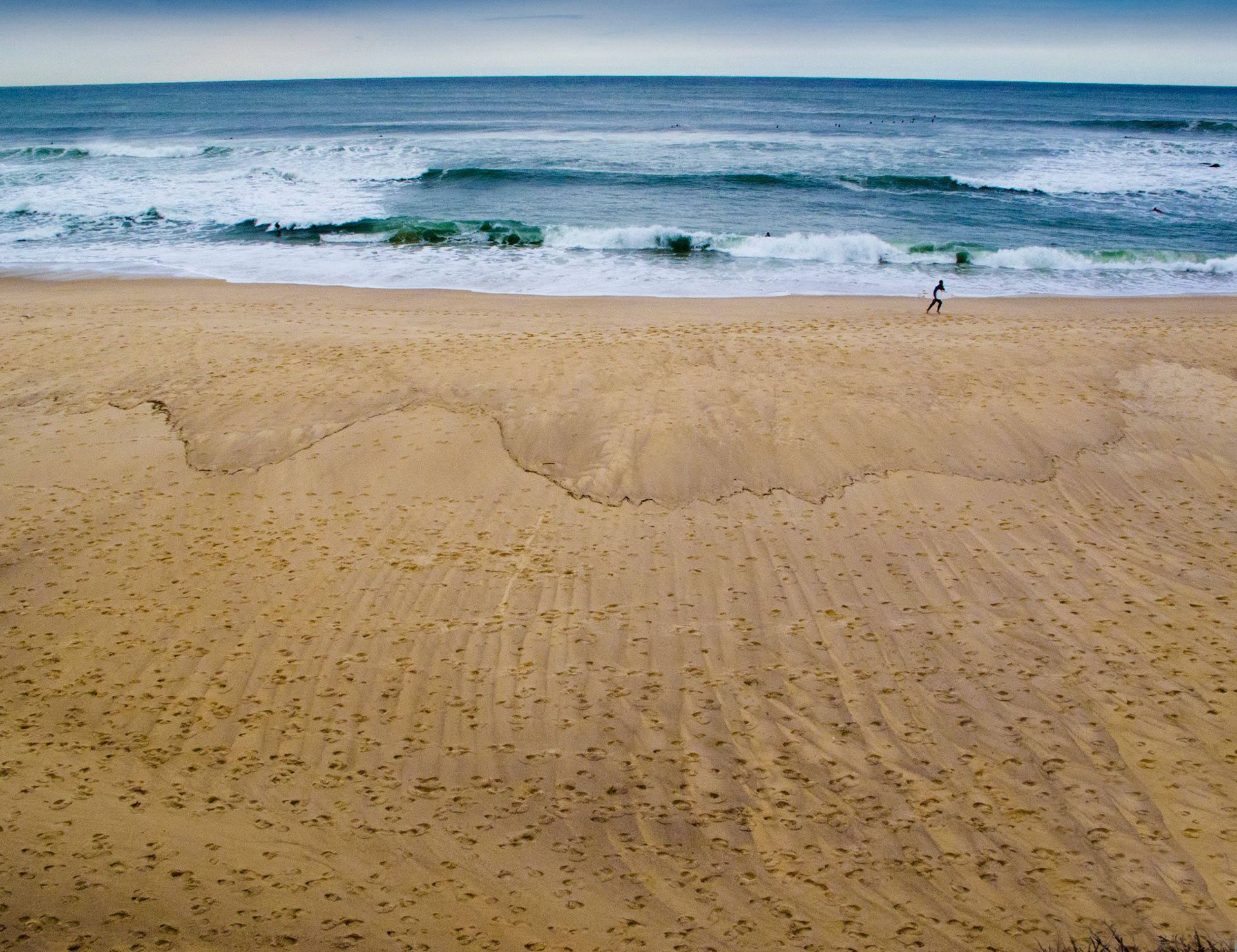 Surfer exiting the water at the end of the day and patterns in the sand.