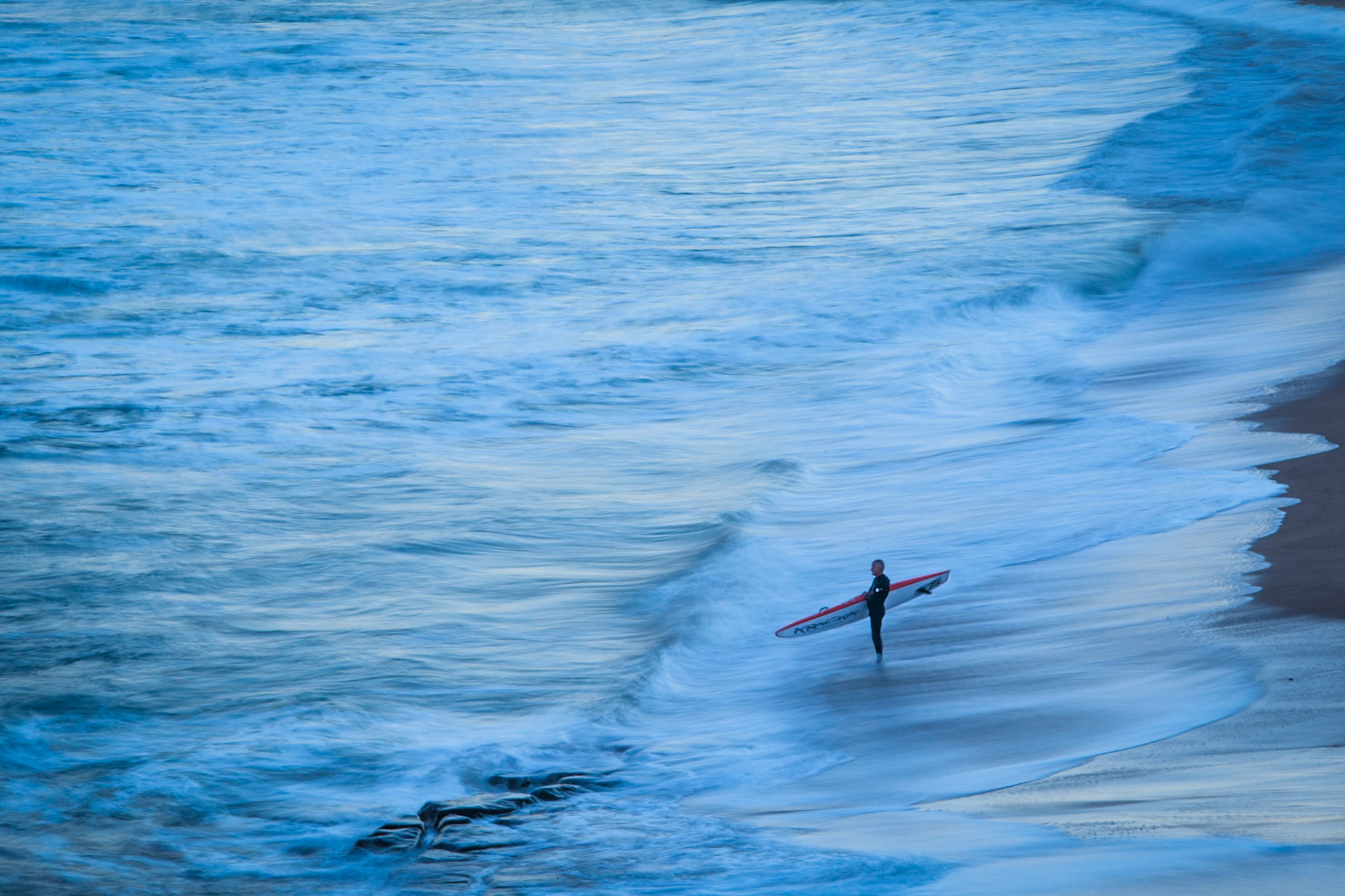 Sunset at Newcastle beach, New South Wales, Australia, showing soft seas and mist and a contemplative surfer.