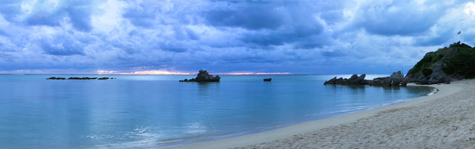 Sunset, outcrop of rocks and the Australian flag flying, from the beach at Pinetrees Lodge, Lord Howe Island