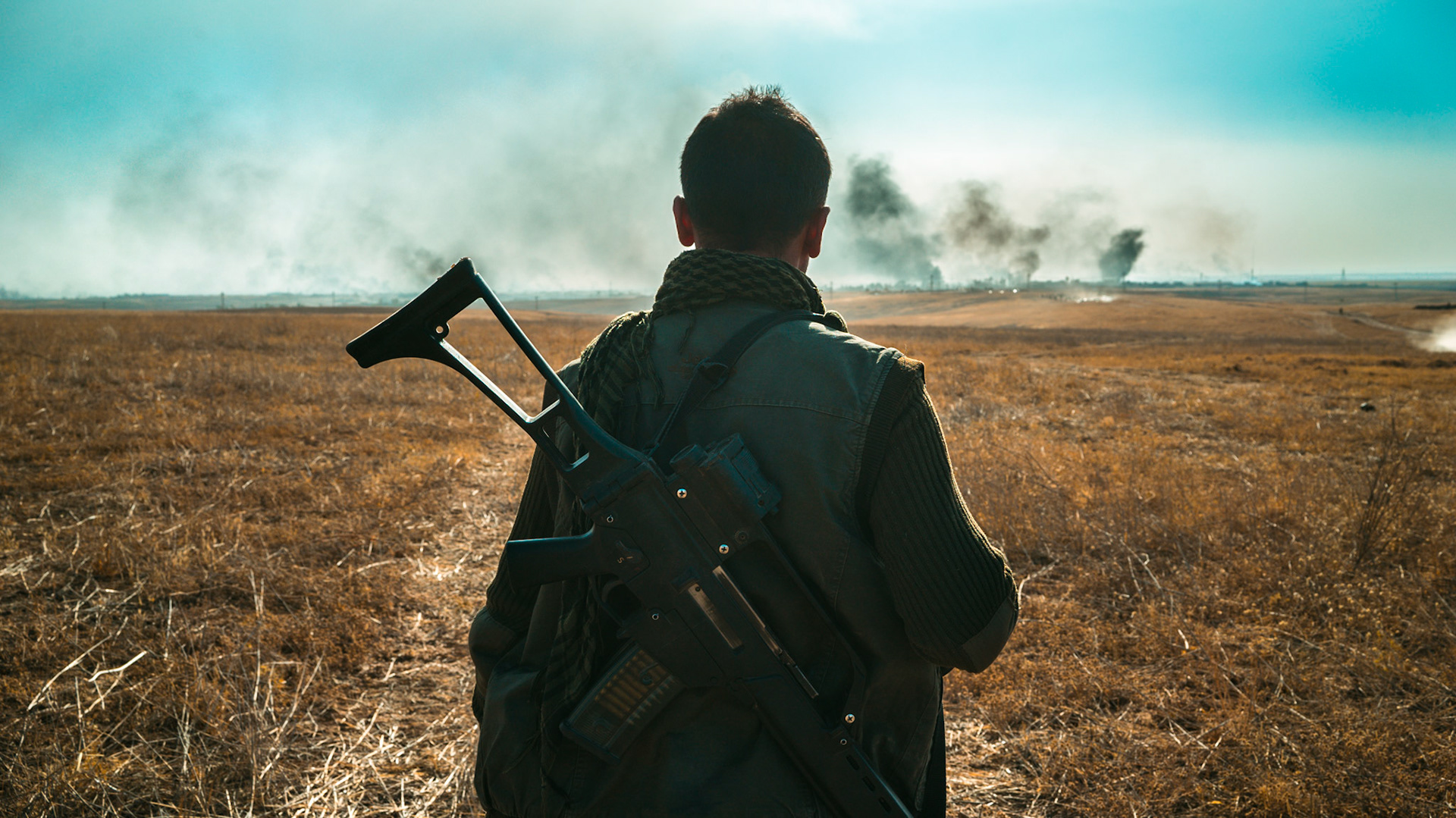 A soldier looks out onto the battlefield with a semi-automatic rifle strapped to his back