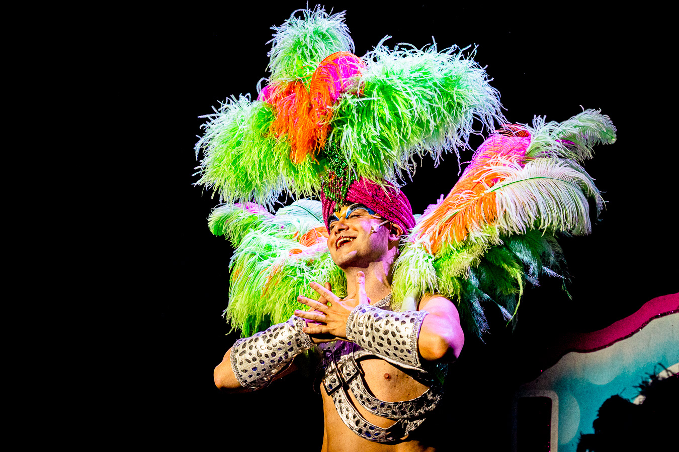 Adam Whitely as drag persona Felicia Jollygoodfellow looking extravagant with plumes of colourful ostrich feathers erupting from their shoulders and head during the song "Confide in Me" - in Chelmsford Amateur Operatic & Dramatic Society's Priscilla, Queen of the Desert, The Musical