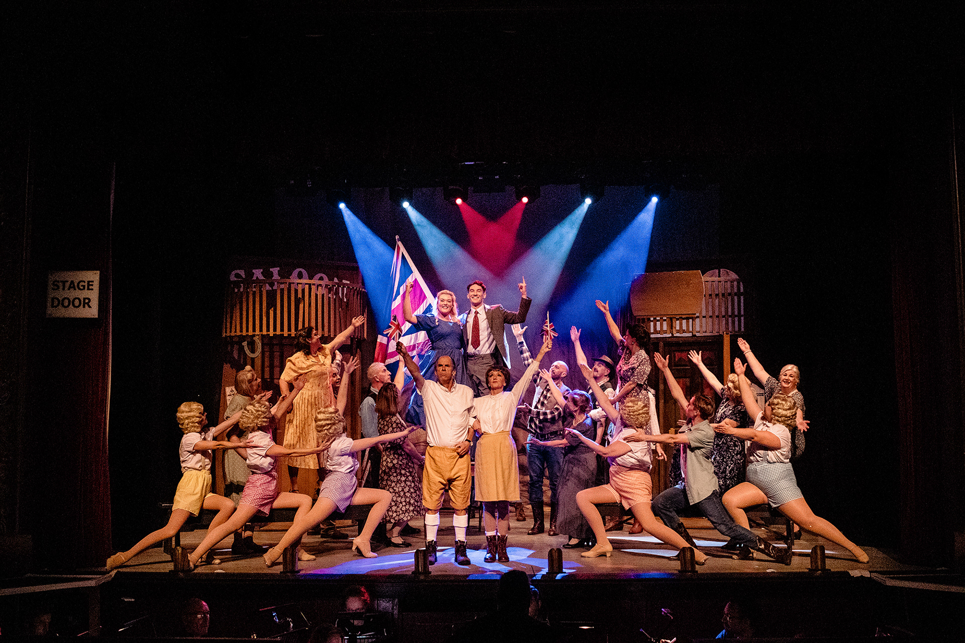 Eugene and Patricia Fodor triumphant after the song "Stiff Upper Lip" surrounded by the rest of the cast, Bobby and Polly raised upon a table behind them with a Union flags waving behind them - Witham Amateur Operatic Society's "Crazy For You".