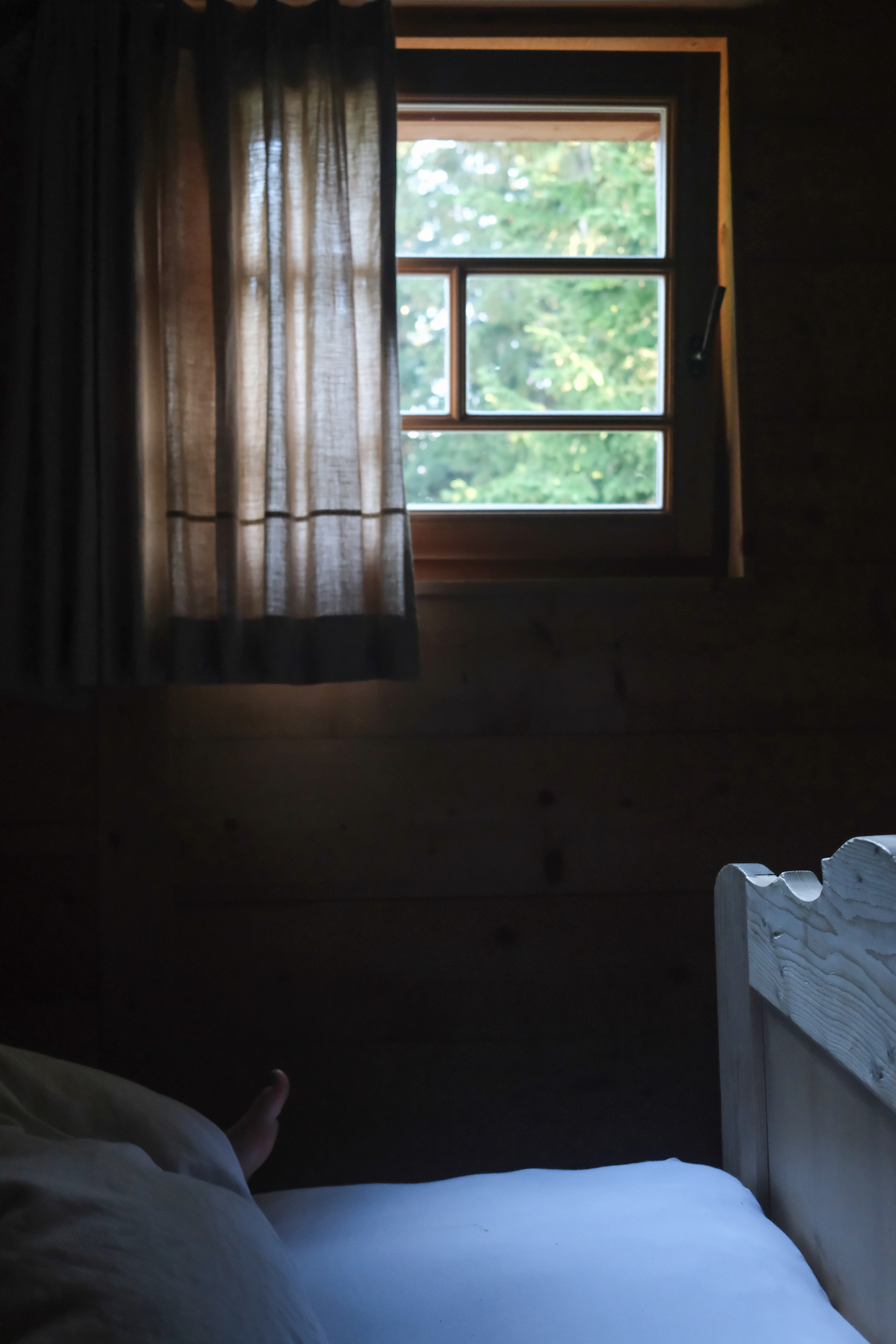 wooden hut from the inside, bedroom with window on the green woods and foot of a child in the bed