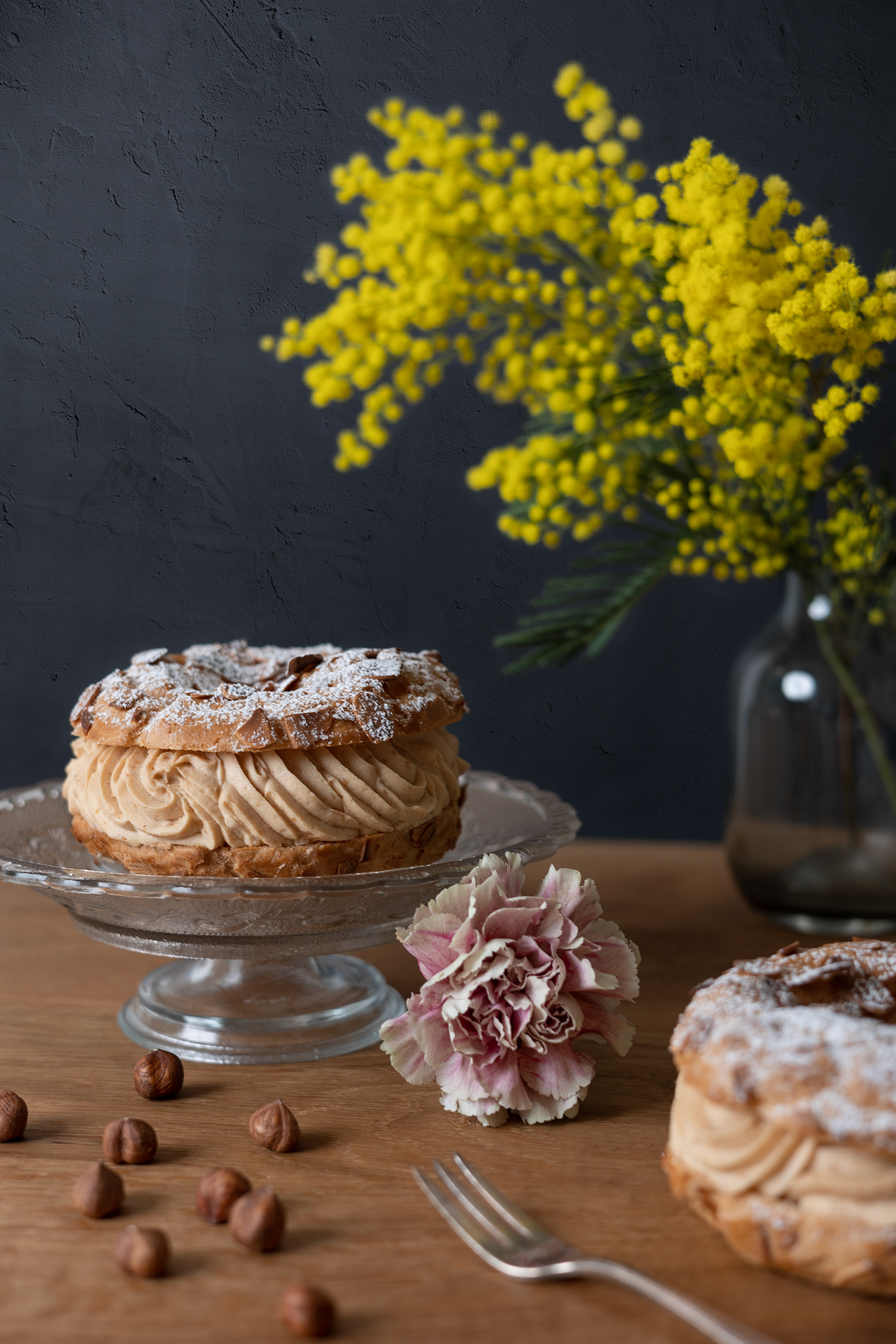 beautiful still life of a Paris-Brest cake with sugar on top and flowers arounf