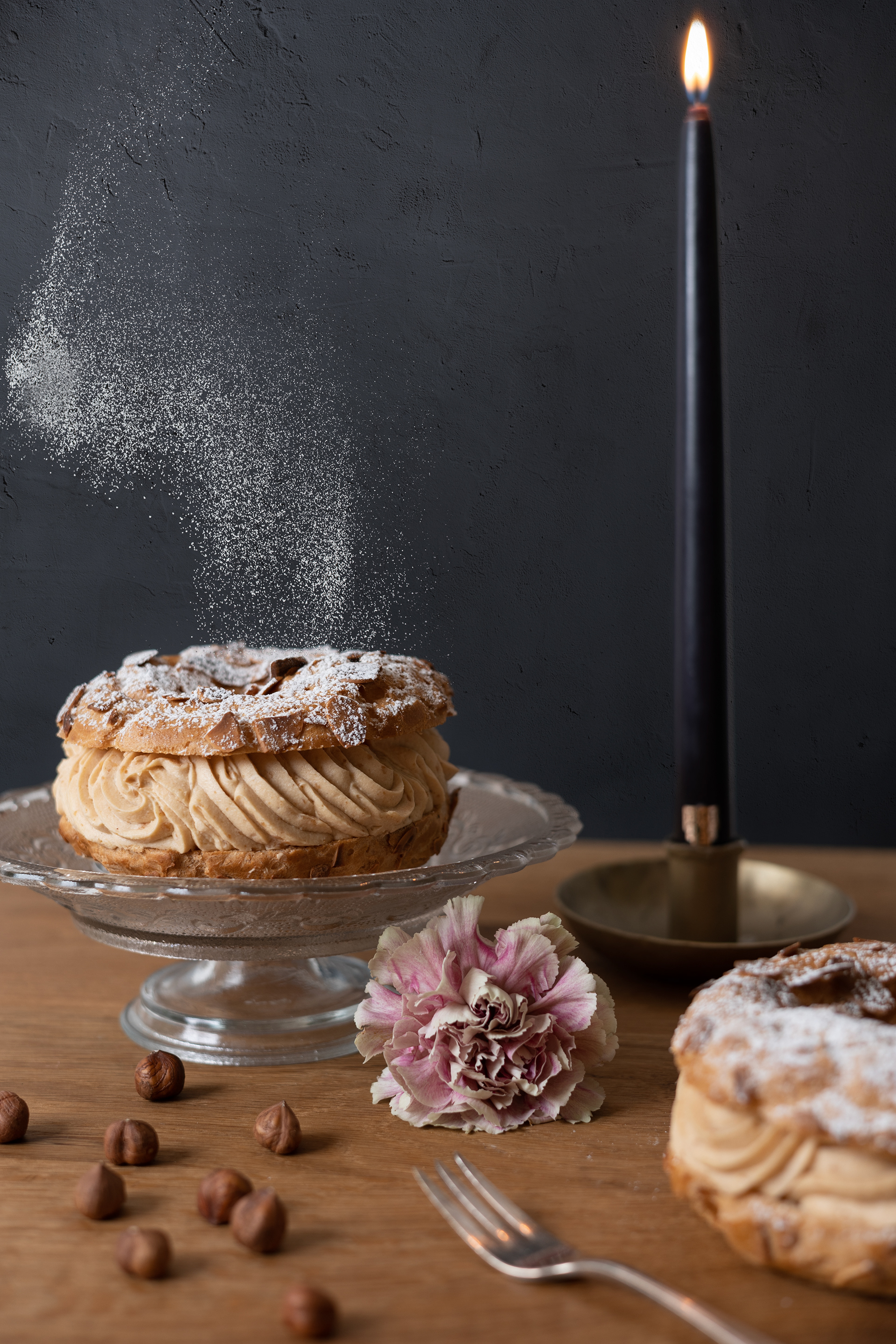 beautiful still life of a Paris-Brest cake with sugar falling on top and flowers around and a black candle