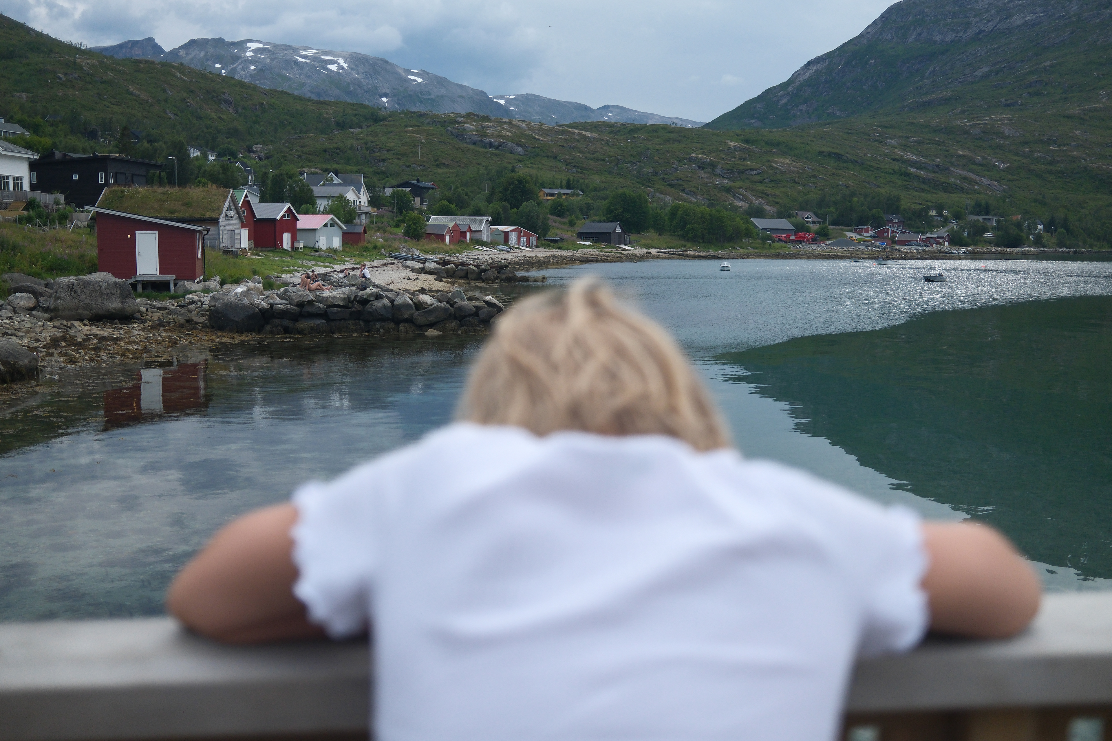 kid looking at the horizon in norway with see, mountains and little red houses
