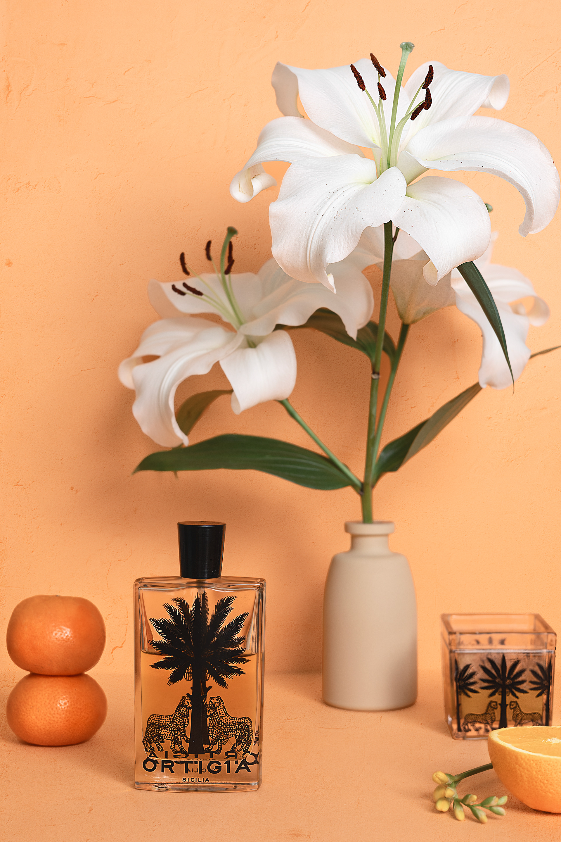 still life with orange background a vase of white Lilium, oranges and the ortigia amber home perfume