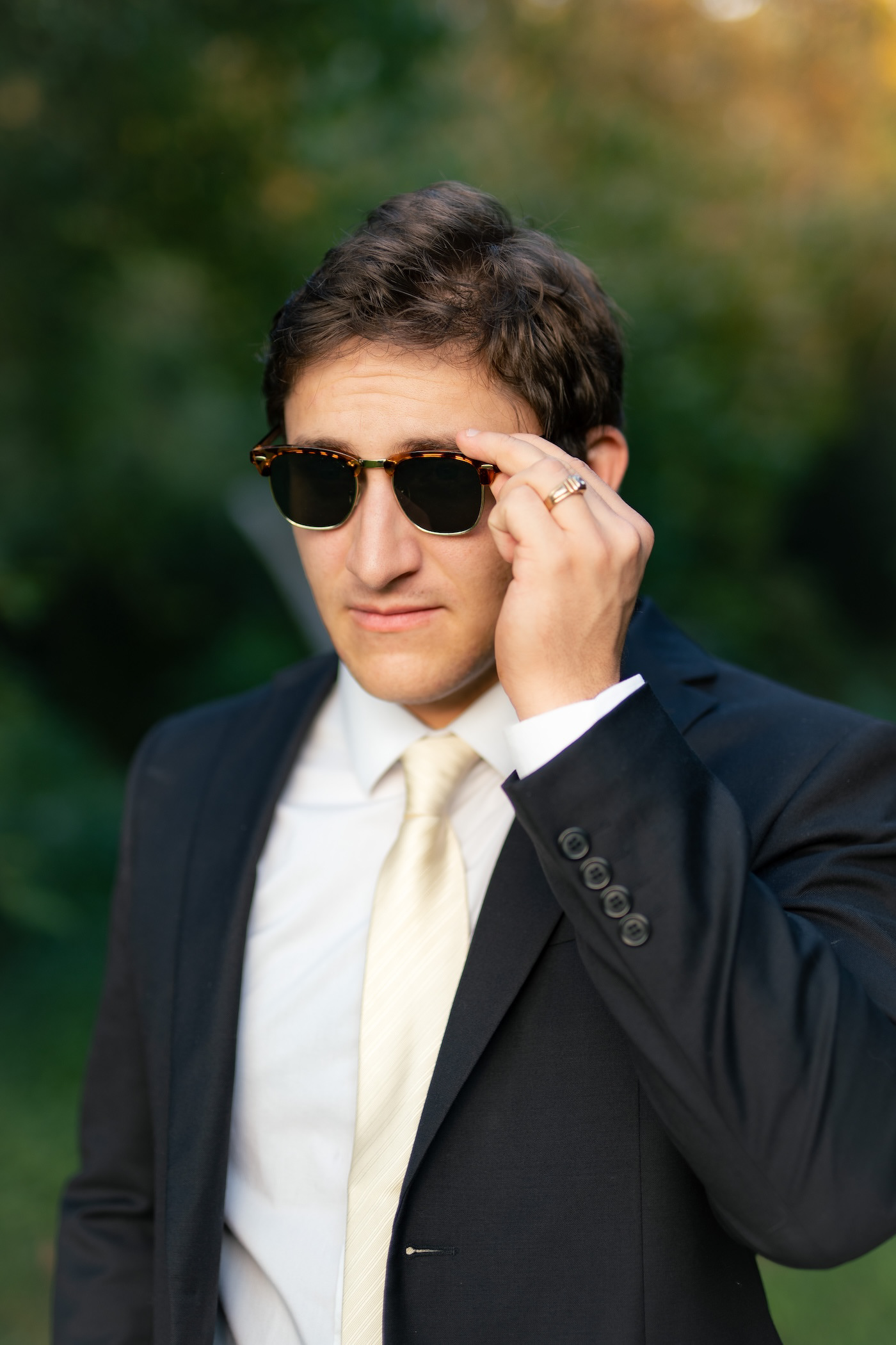 Profile portrait of the groom wearing sunglasses and displaying his wedding ring on his hand.
