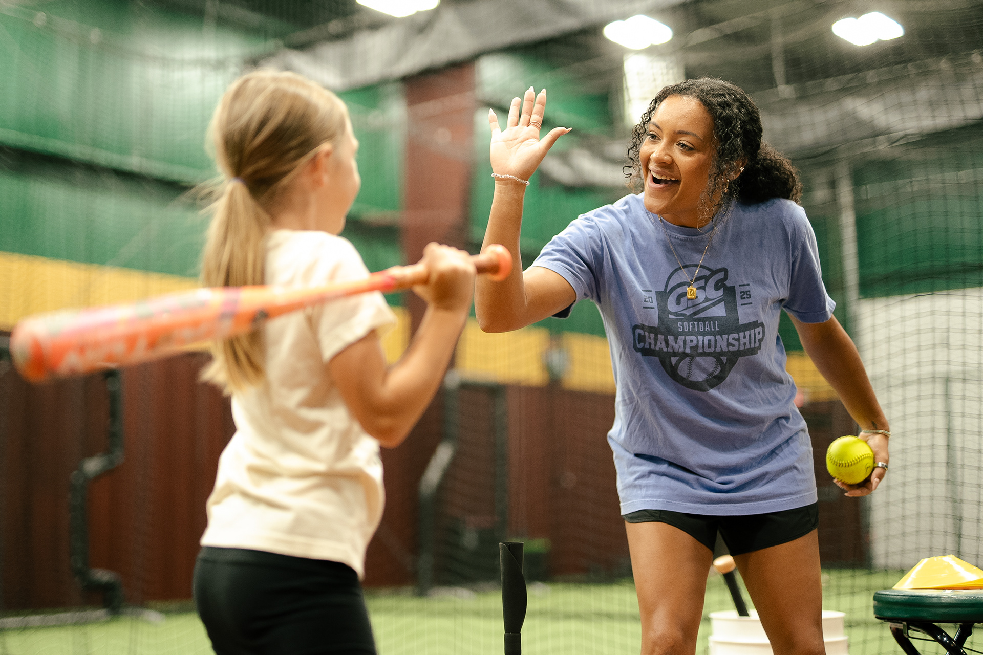 D-BAT Rocket City instructor high-fiving a young softball player during a hitting lesson as she practices off a tee.