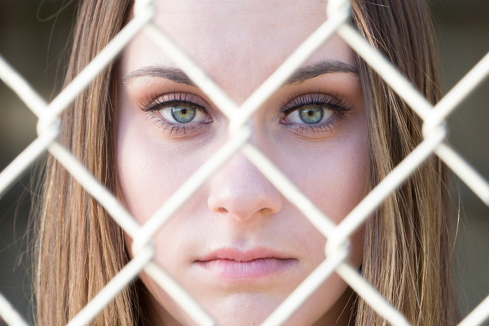 Sports photograph of softball player looking through a fence in Clovis, CA