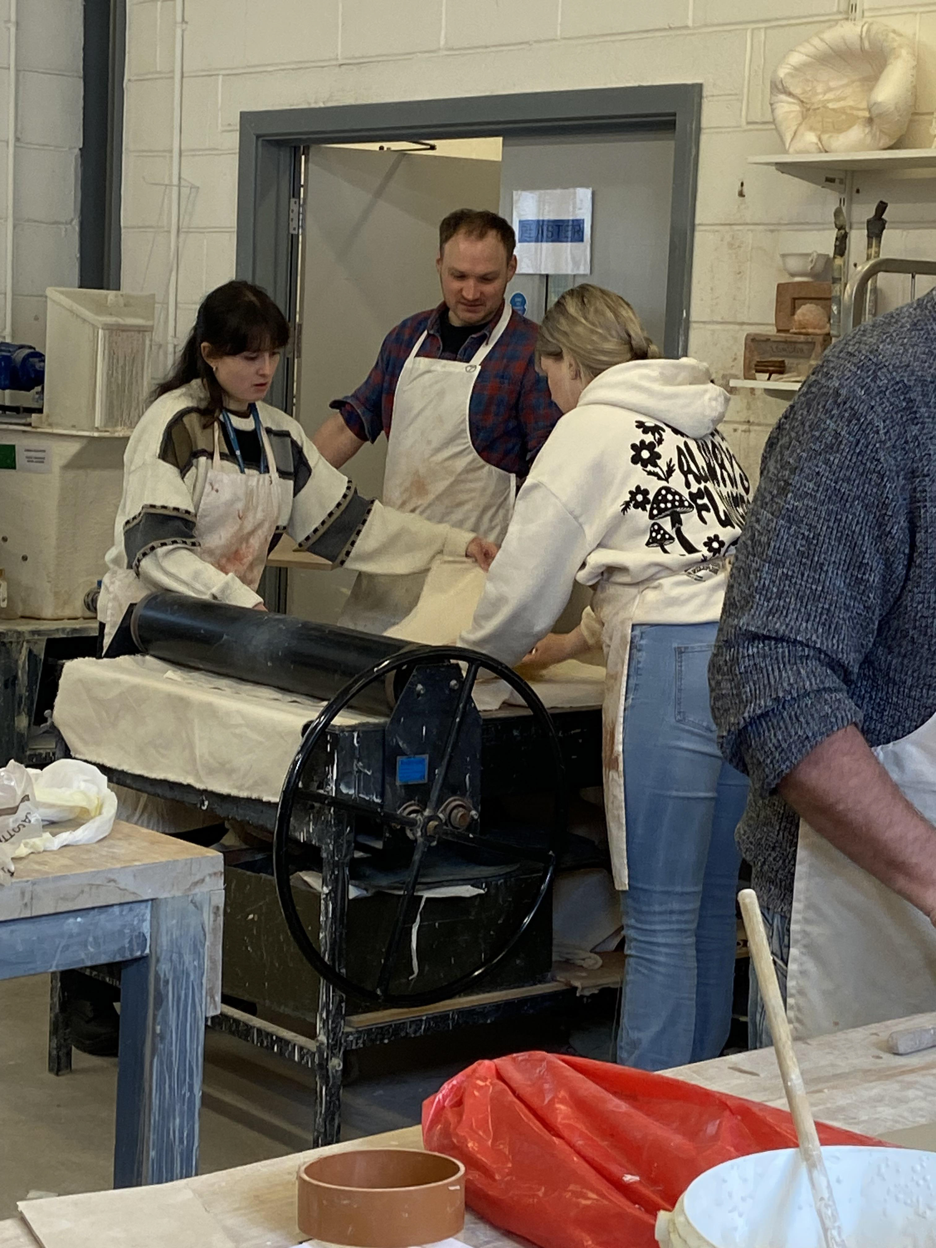 Becky and Gemma flattening their clay through the slab roller