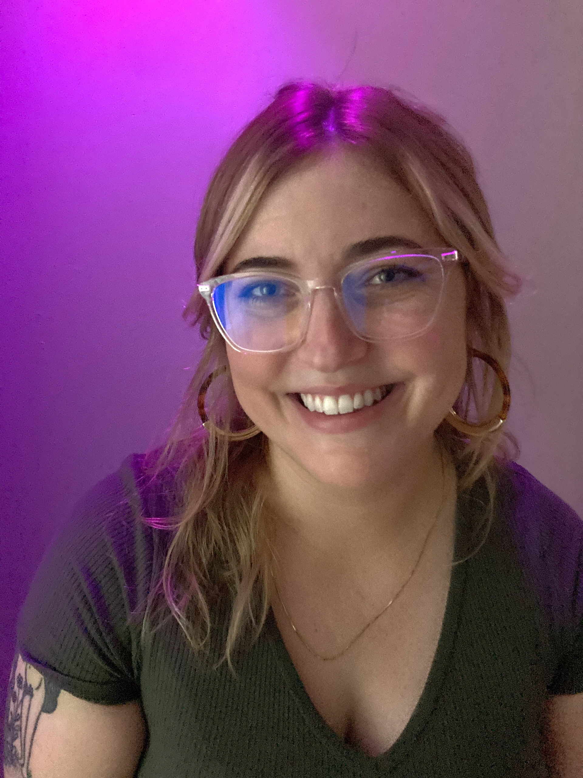 Woman smiling, wearing glasses, with bisexual lighting.