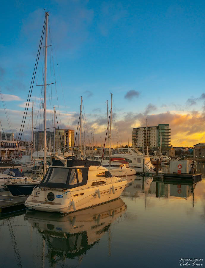 Small boats and yachts are reflected in the still waters of Sutton Harbour during sunrise over Plymouth.