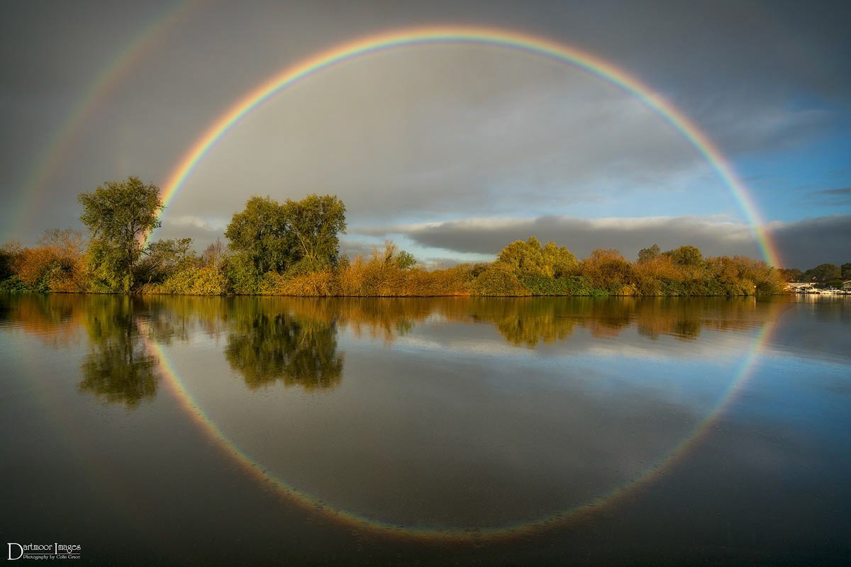 Rain begins to fall on the River Yare in Blundall in Norfolk as a combination of heavy cloud and direct sunlight produce a complete rainbow over the river.