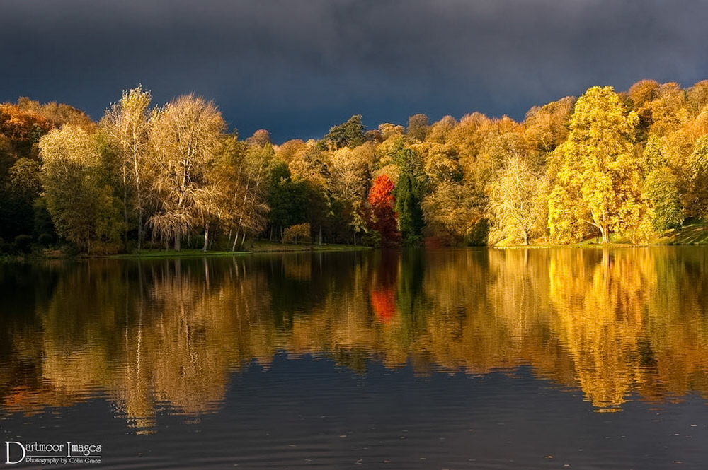 Heavy storm clouds over Stourhead Gardens in Wiltshire. The low sun below the clouds light up the trees that surround the lake of this National Trust property in Wiltshire.