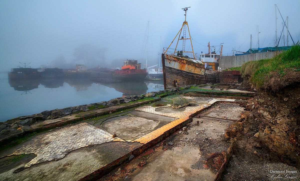 A light mist covers old boats and wrecks moored alongside Huggins Brothers boatyard in Torpoint Cornwall.