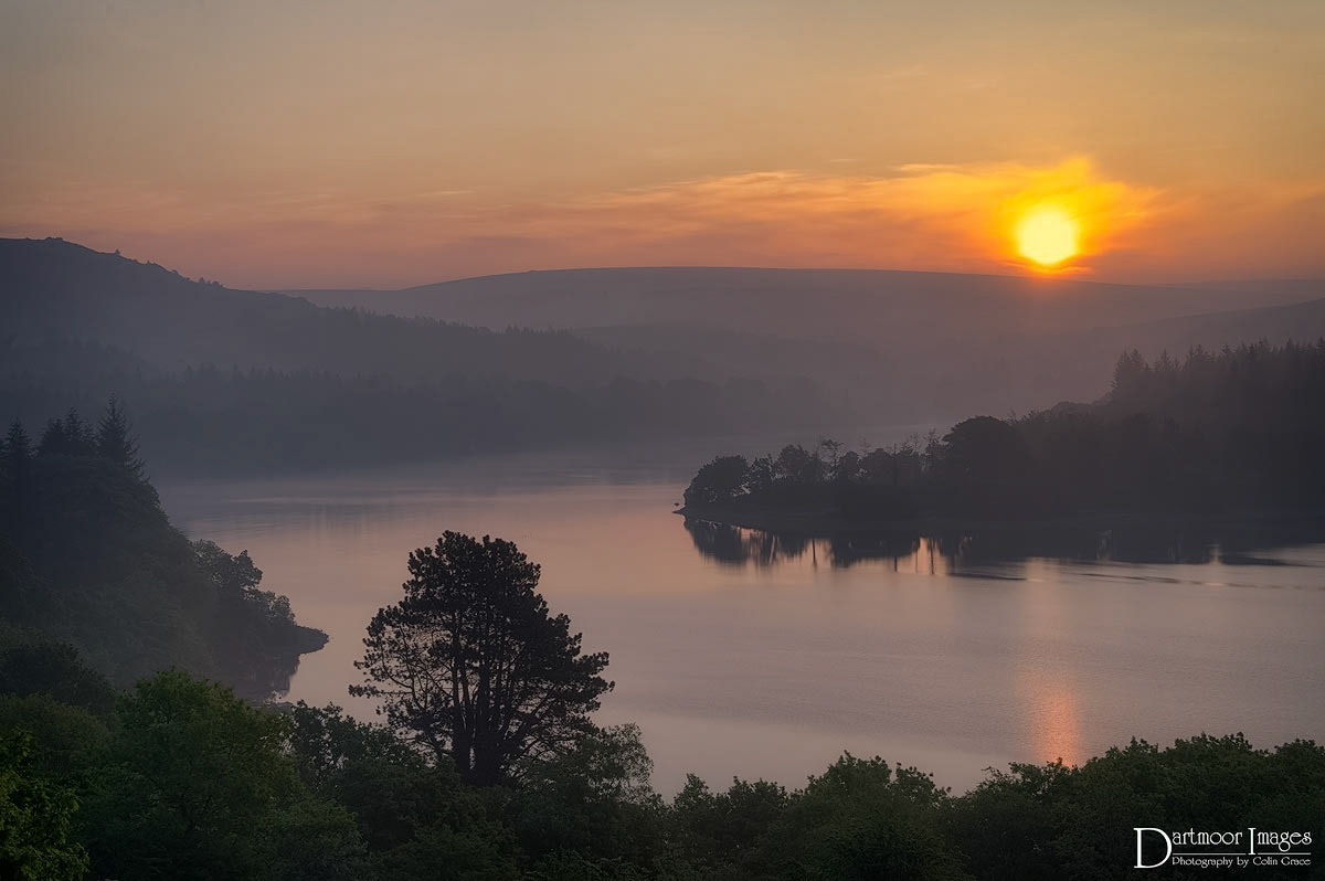 The first light of the rising sun over Dartmoor is reflected in the still waters of Burrator Reservoir.