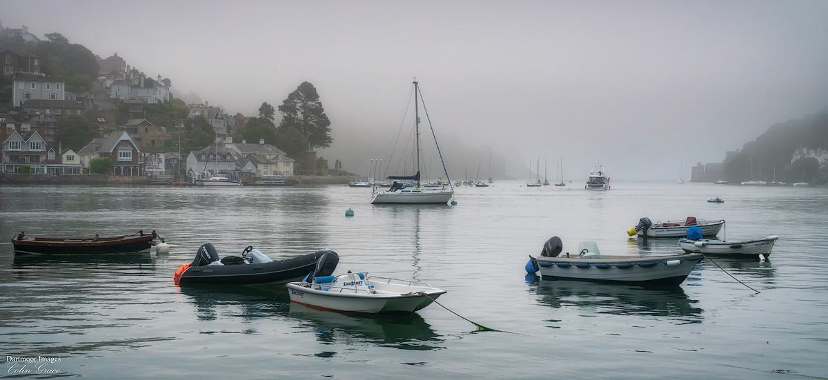 A small motor yacht heads towards Dartmouth and Kingswear Castles at the mouth of the River Dart during a misty start to the morning over Dartmouth in Devon.