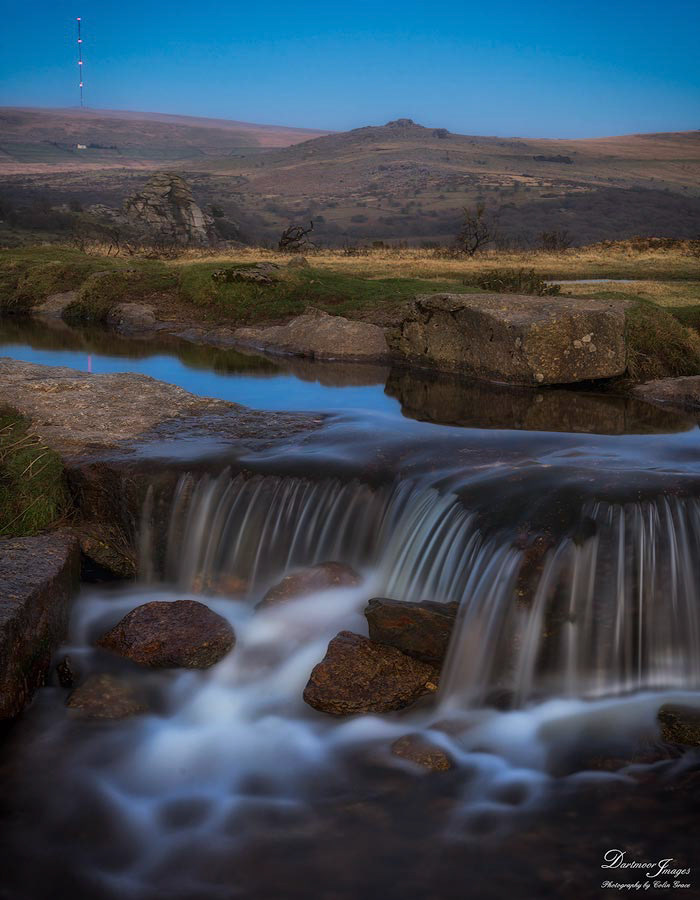 The Grimstone and Sortridge Leat falls gently over rocks as it makes its way past Windy Post at Merrivale on Dartmoor National Park. Vixen Tor, Kings Tor and North Hessary Tor, with its distinctve TV mast can be seen in the distance.