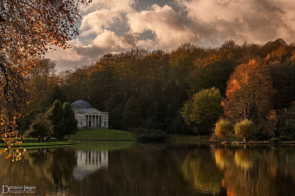 Heavy clouds skud across the sky above Stourhead Gardens as the low autumn sun casts its remaining light on the trees and island that are one of the features of this National Trust atrraction.