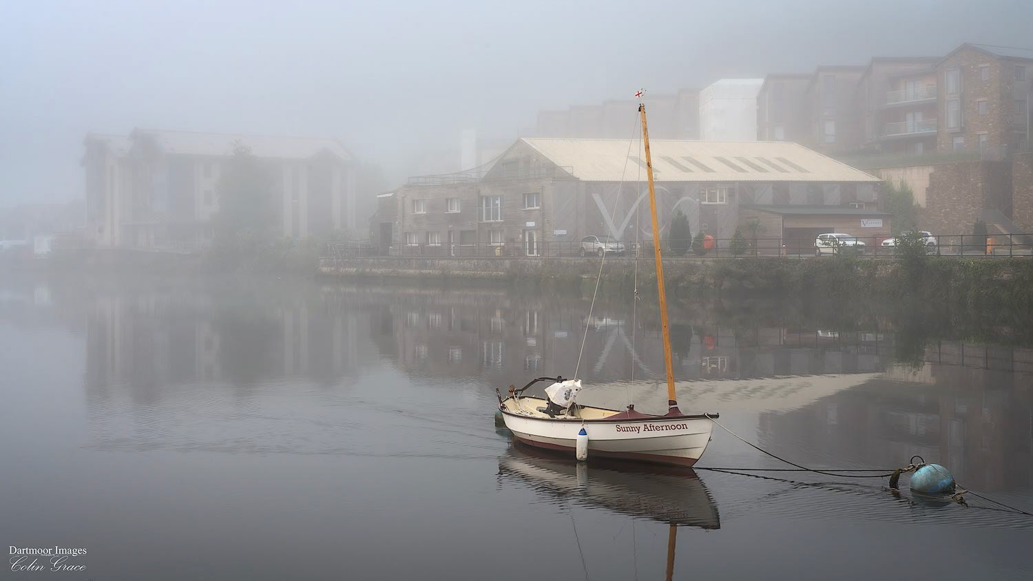 A small boat called Sunny Afternoon sits at its moorings on the River Dart during a misty sunrise over Totnes in Devon.
