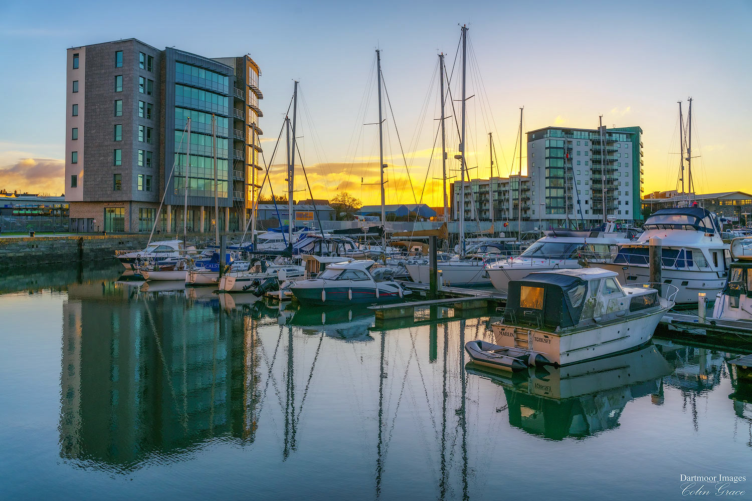 The rising sun adds colour to a near cloudless sky over Plymouth as small boats and yachts sit idle at their moorings in Sutton Harbour.
