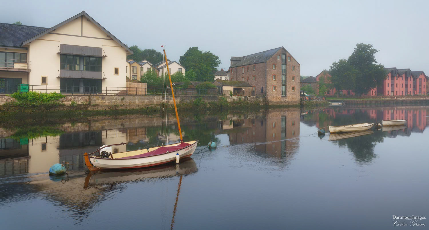 Buildings that line the water front are refelcted in the still waters of the River Dart as a slight mist hangs in the air over Totne in Devon.