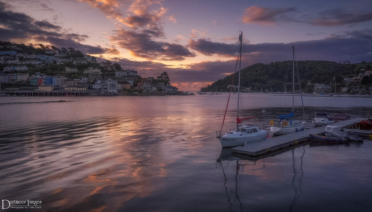 Small boats and yachts moored outside the Dartmouth Yacht Club rock gently on their moorings as the sun begins to rise over Kingswear and Dartmouth in Devon.