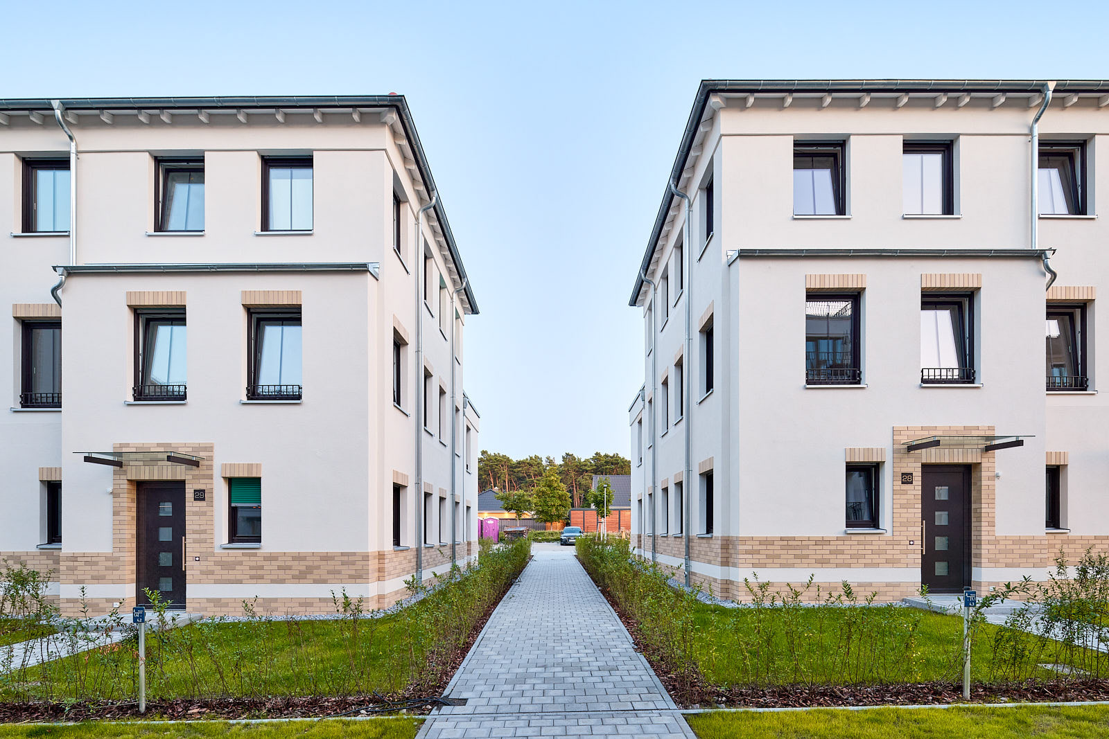 Gerader Fußweg zwischen zwei Reihenhauszeilen am Rosenanger mit hellen Fassaden, dunklen Eingangstüren und niedrigen Hecken.