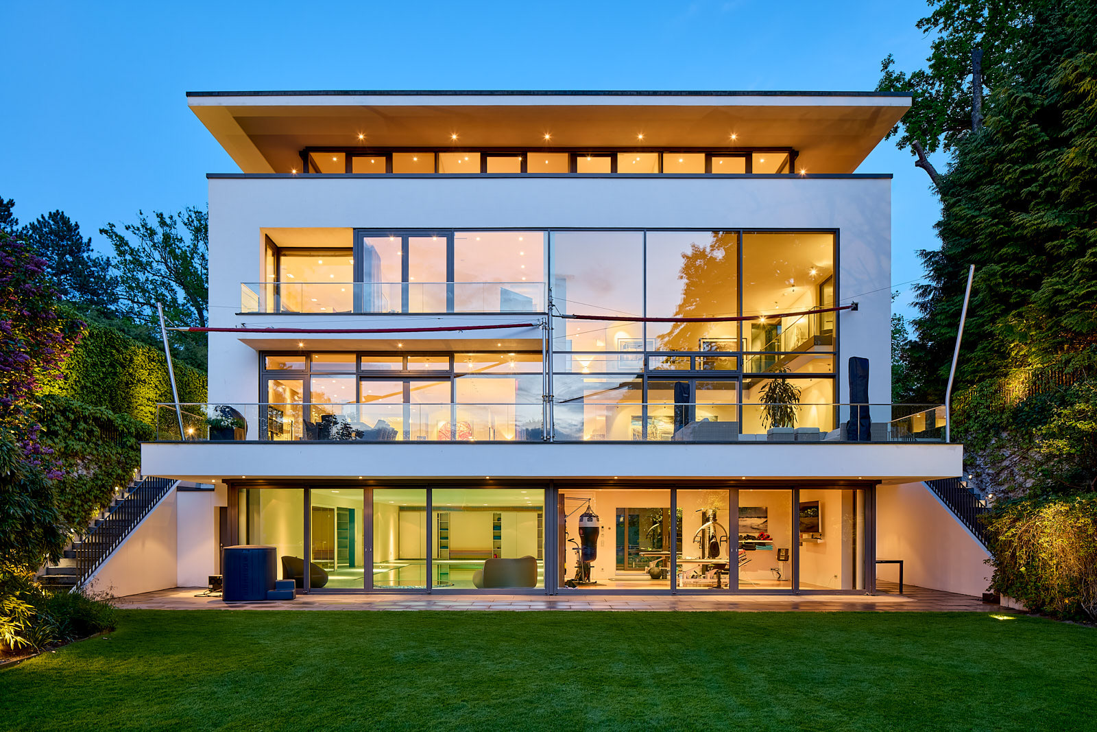 Modernes Wohnhaus bei Abendlicht mit großflächiger Verglasung und warm beleuchteten Innenräumen.