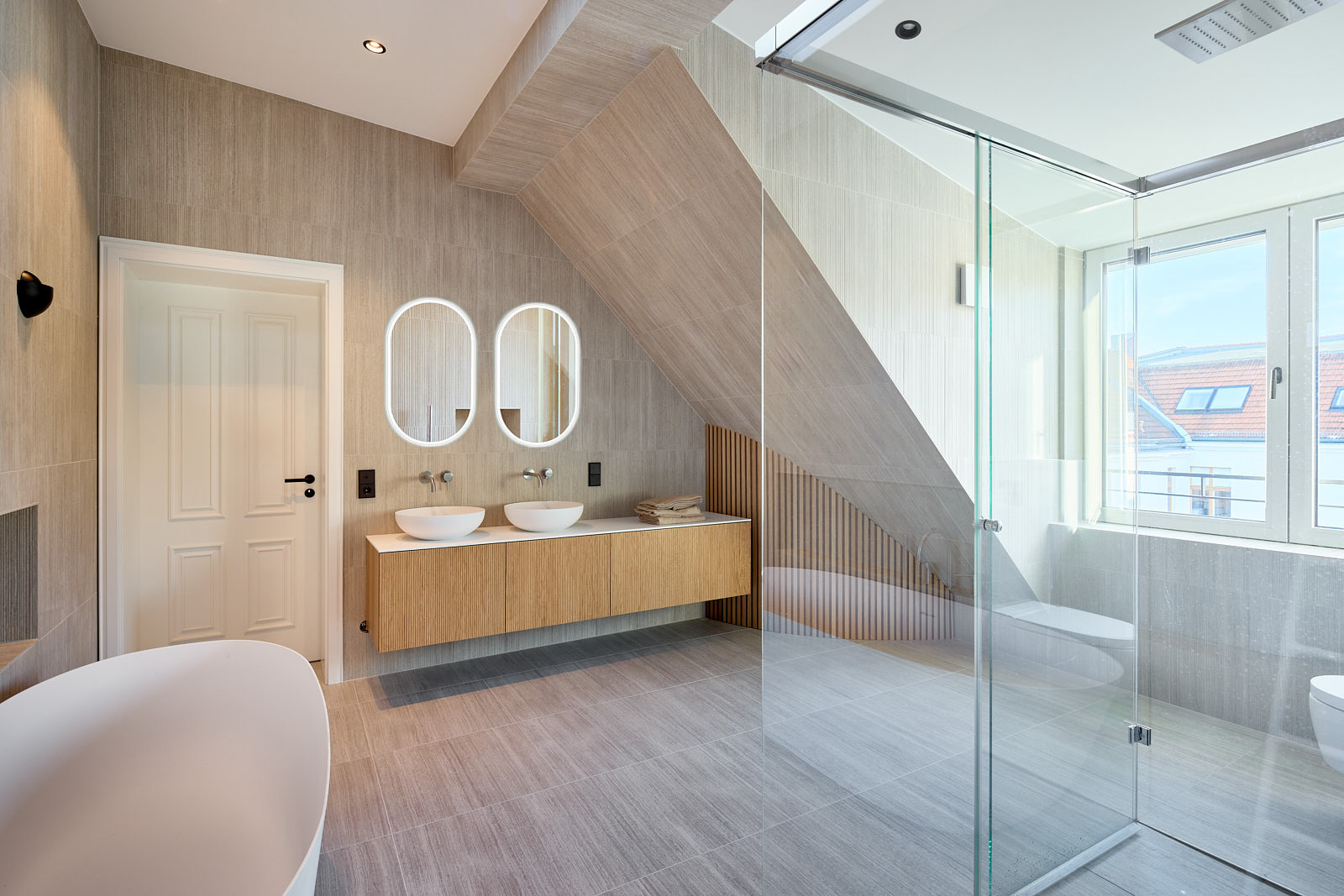 Großzügiges Badezimmer mit freistehender Badewanne, langer Waschtischanlage, zwei Spiegeln und raumhoher Verglasung.