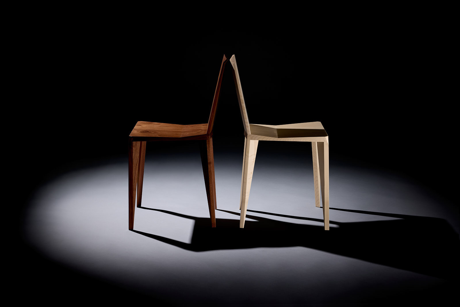 Zwei handgefertigte Lounge Chairs von FISCH / Jacob Cranz in dunklem und hellem Holz vor schwarzer Studiokulisse.