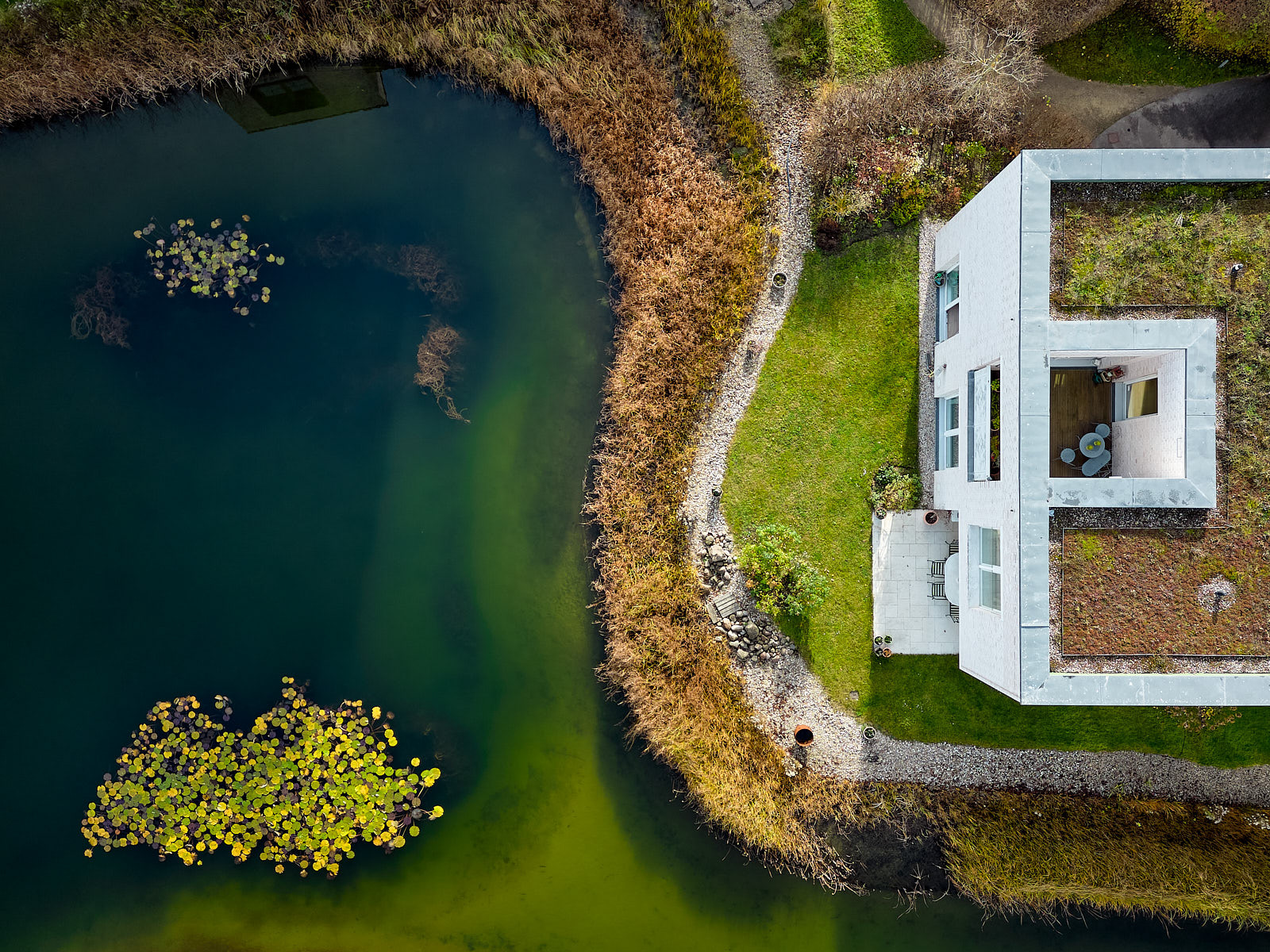 Luftaufnahme eines modernen weißen Wohnhauses direkt an einer landschaftlich gestalteten Wasserfläche.